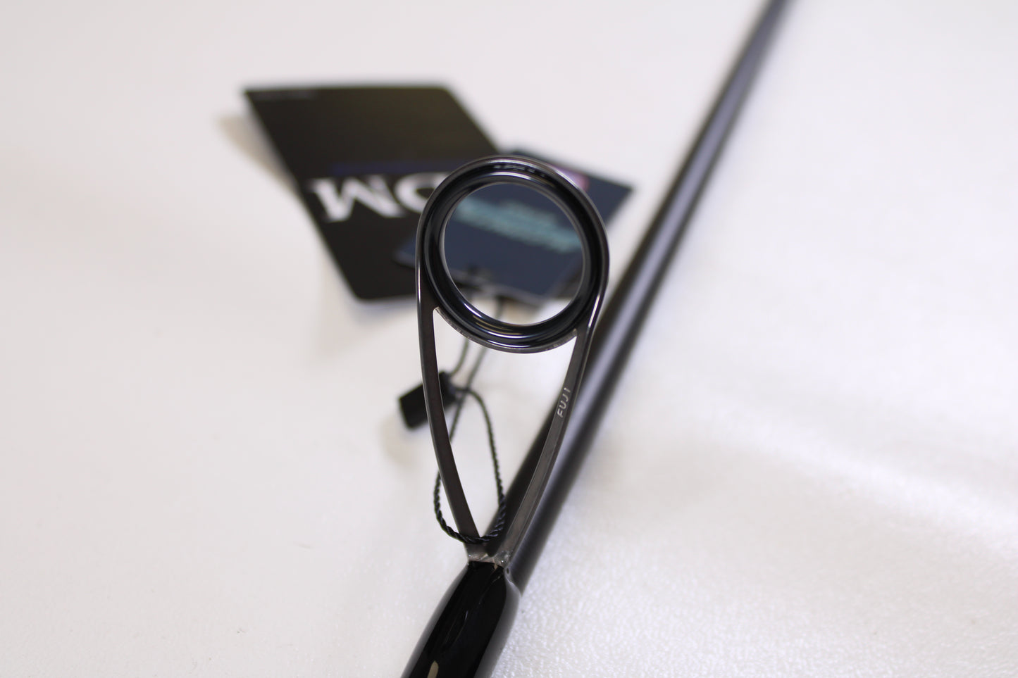 Close-up of an ODM Rods Genesis Inshore BXGX 761MS 7'6" Medium spinning rod guide ring, tags attached in the background—ideal for those looking to trade in or earn store credit on used fishing gear.