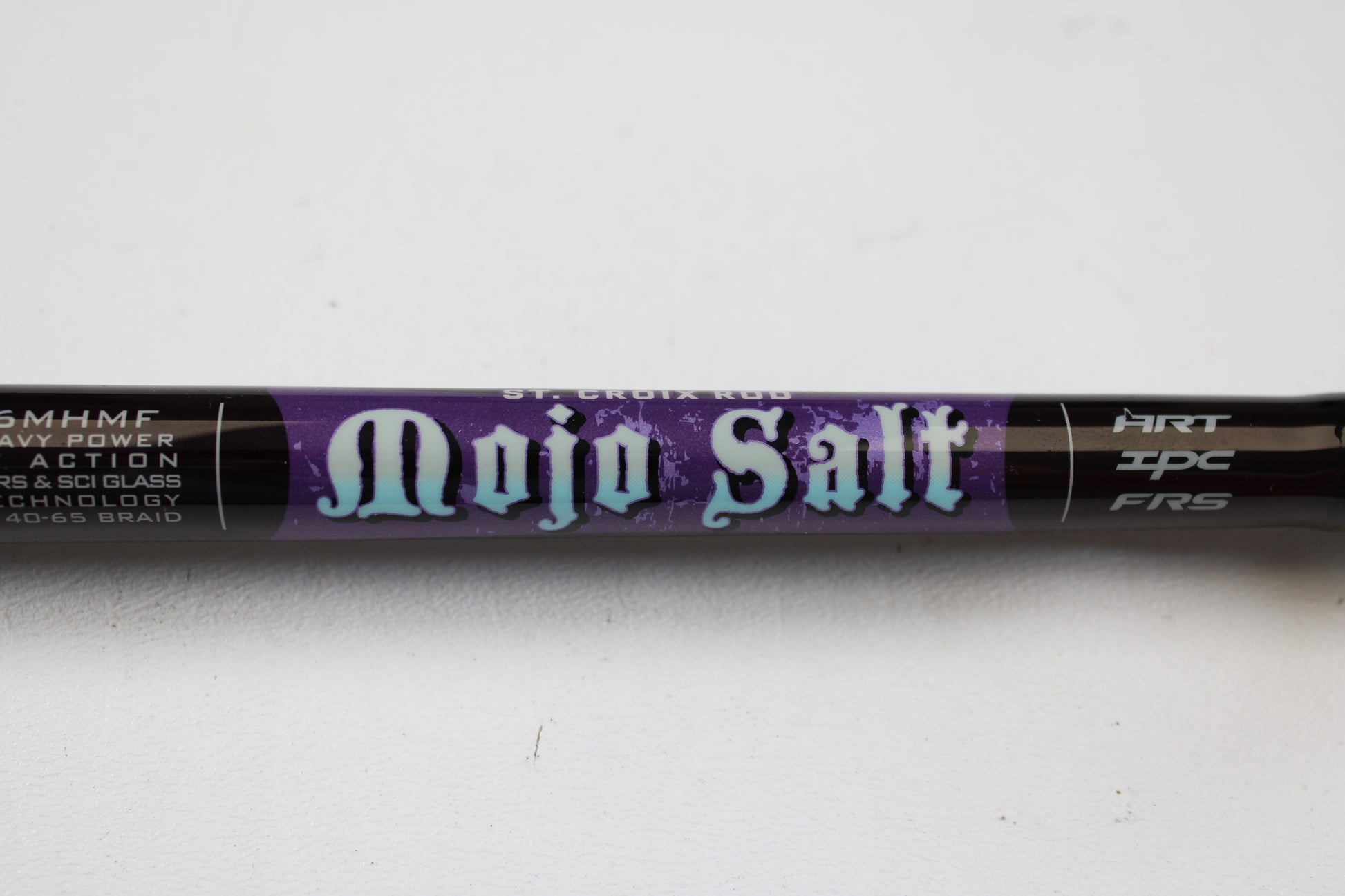 Close-up of a St. Croix Mojo Salt MSWC76MHMF 7'6" Medium Heavy Used Casting Rod in mint condition. Trade in your gear with our Rod and Reel Trade-In Program for store credit. Purple background highlights white and blue text.