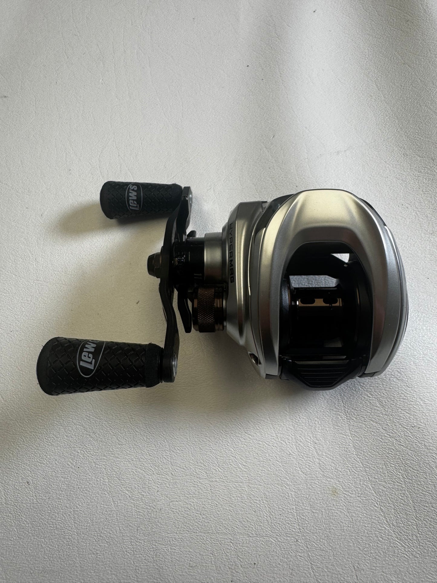 A sleek, modern Lew's HyperMag TLH1XHLG2 baitcasting reel with two black handles rests on a light surface, showcasing the brand logo. Perfect for the Rod and Reel Trade-In Program, this excellent condition gear can earn valuable store credit.