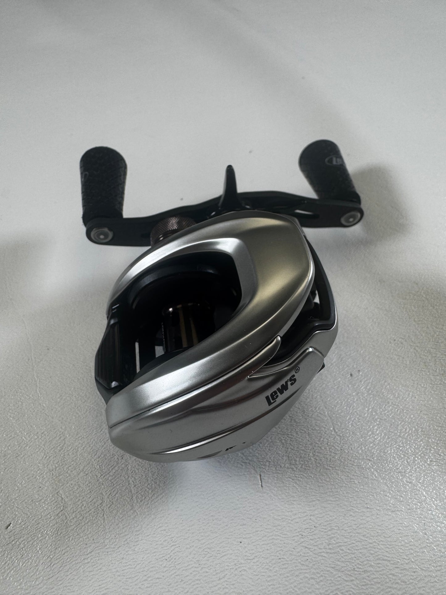 A sleek, silver Lew's HyperMag TLH1XHLG2 casting reel, in excellent condition, rests on a white surface. Its black handle with textured grips is perfect for fishing adventures. Trade in your used gear and earn store credit to upgrade your fishing experience.