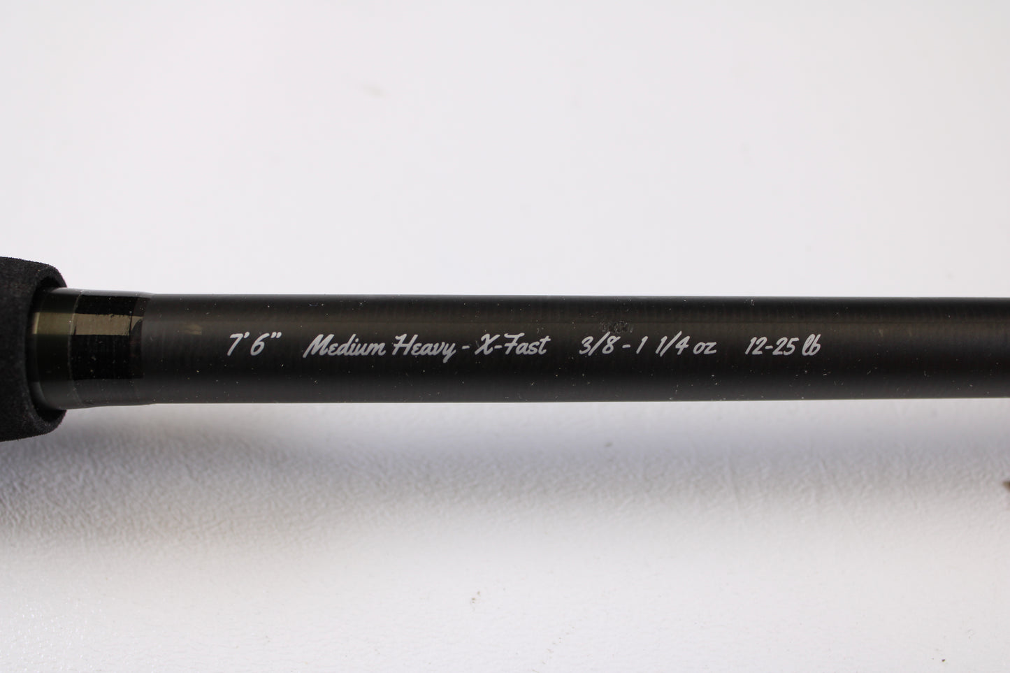 A close-up of the 13 Fishing Muse 7'6" Medium Heavy Used Casting Rod in excellent condition shows white specs: "7'6" Medium Heavy - X-Fast 3/8 - 1 1/4 oz 12-25 lb," ideal for our rod and reel trade-in program, against a light background.