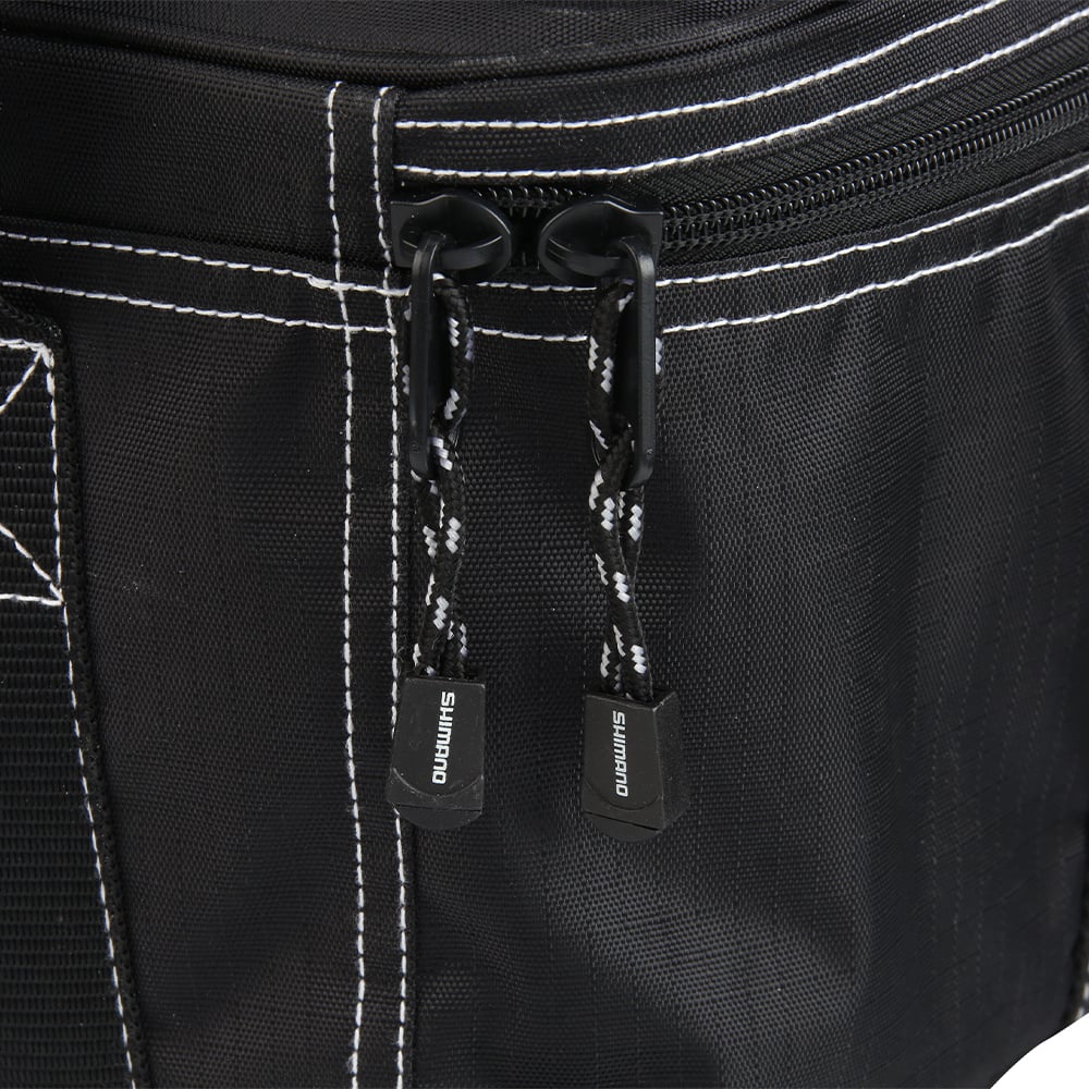 Close-up of two black and white corrosion-resistant zippers with "SHIMANO" branding on the Shimano Bhaltair Reel Bag Medium, designed to protect your fishing reels and featuring visible white stitching.