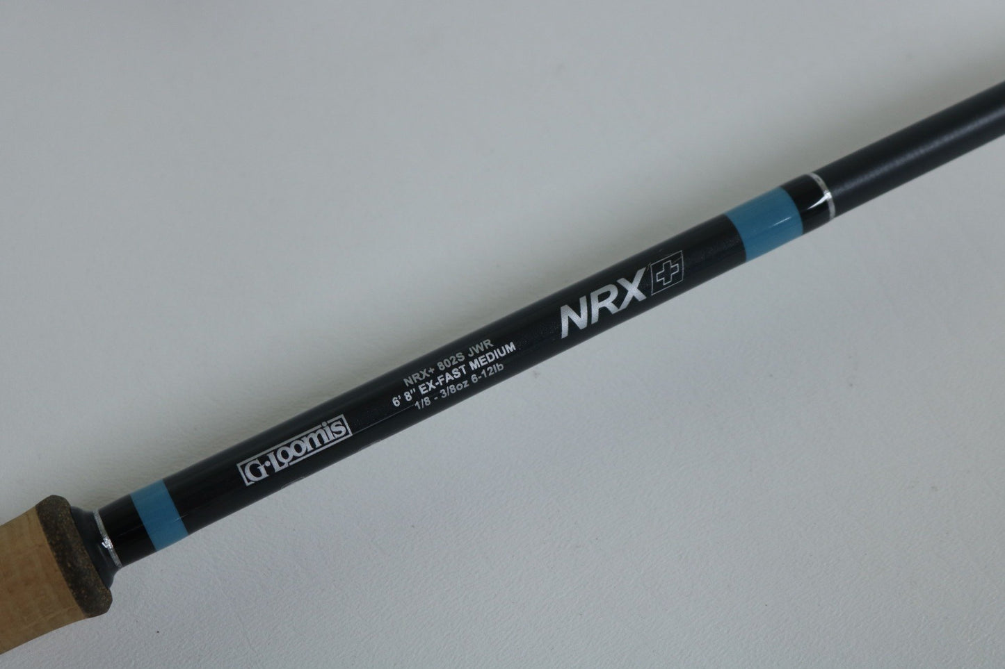 A close-up of a G. Loomis NRX+ 802S JWR Used Spinning Rod in mint condition shows the handle and branding against a white background—ideal for those interested in our rod and reel trade-in program.