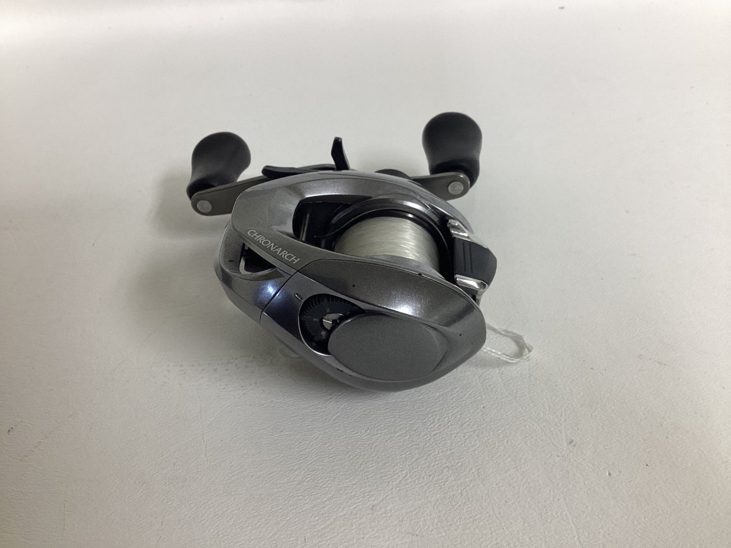 A Shimano Chronarch MGL CHMGL150HG used baitcasting reel in excellent condition with black handles and white fishing line, shown on a plain white surface.