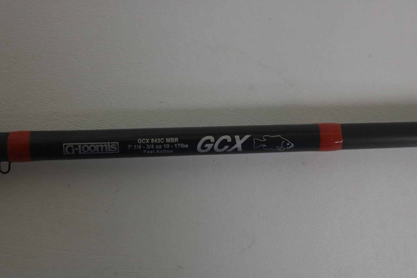 Close-up of a G. Loomis GCX 843C MBR rod in black with red accents, labeled "7'1," 3/16-5/8 oz, 10-17 lbs," and "Fast Action," featuring a fish icon.