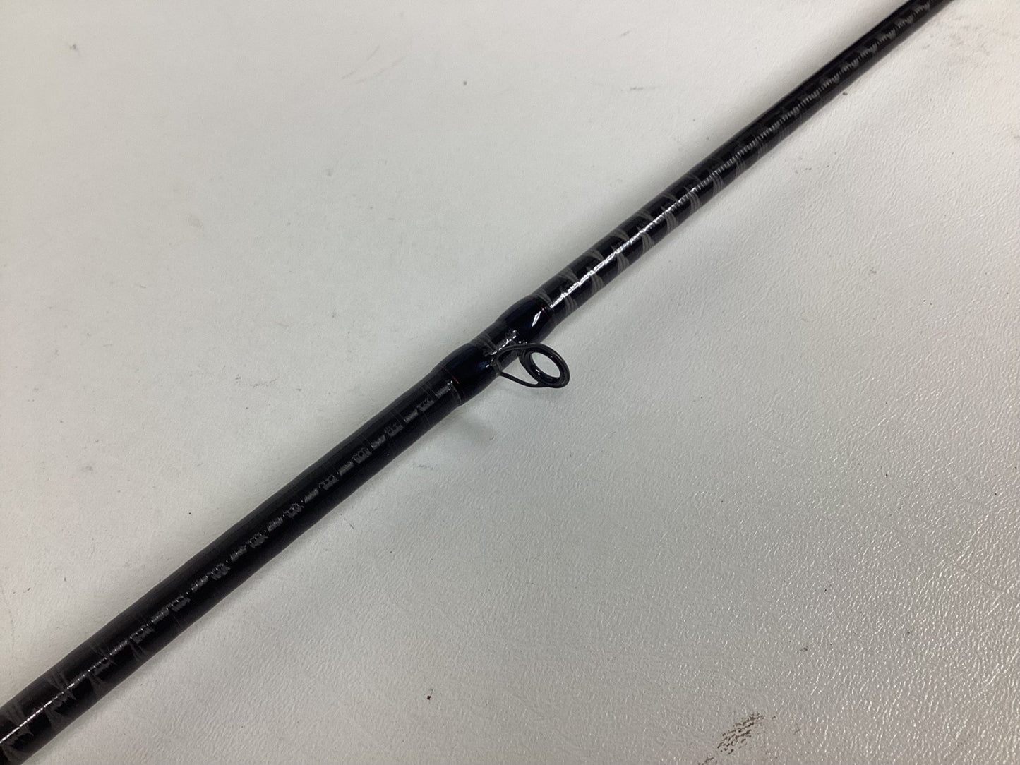 A close-up of the Shimano Zodias ZDC72MLBFSA Used Casting Rod in excellent condition, featuring part of the black rod and a single line guide lying on a white surface.