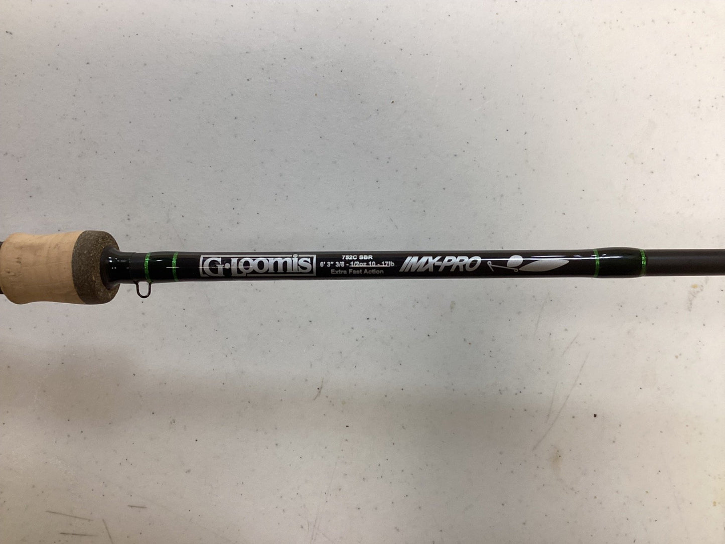 A G. Loomis IMX-Pro 752C SBR Used Casting Rod in excellent condition, showing specs and a cork handle, rests on a white surface. Ideal for our Rod and Reel Trade-In Program—exchange your used gear for store credit.