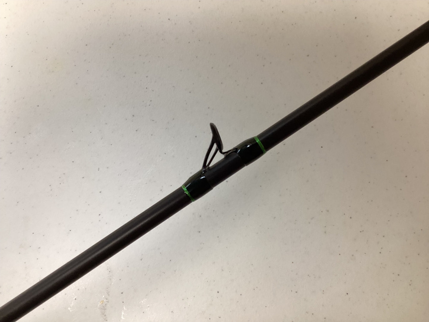 A close-up of a G. Loomis IMX-Pro 752C SBR Used Casting Rod in excellent condition shows a line guide tied with green thread against a light, speckled background.