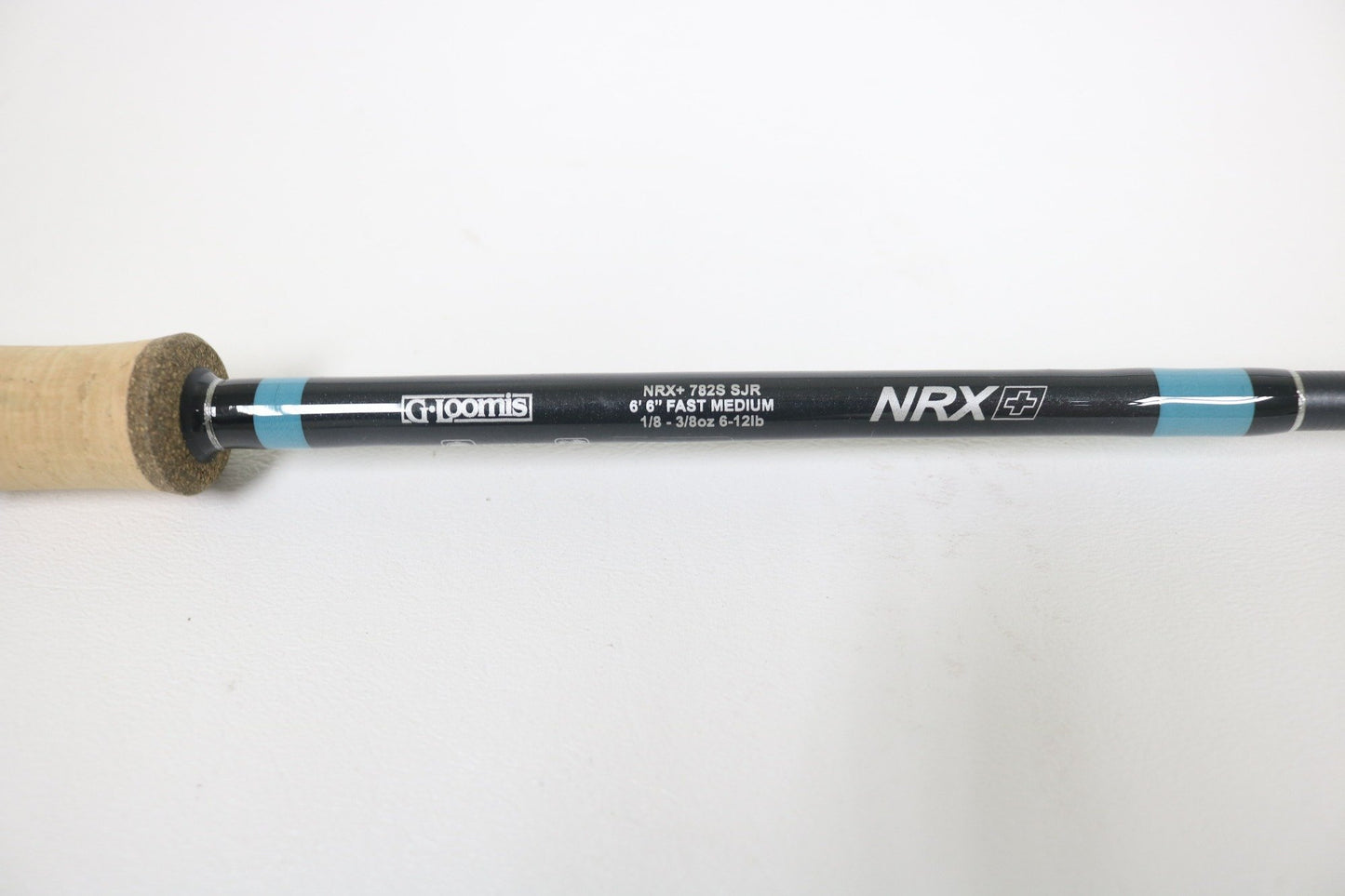 A close-up shows a G. Loomis NRX+ 782s SJR 6'6" Medium Used Spinning Rod in excellent condition, ideal for Rod and Reel Trade-In or store credit, featuring a black and blue shaft with cork handle.