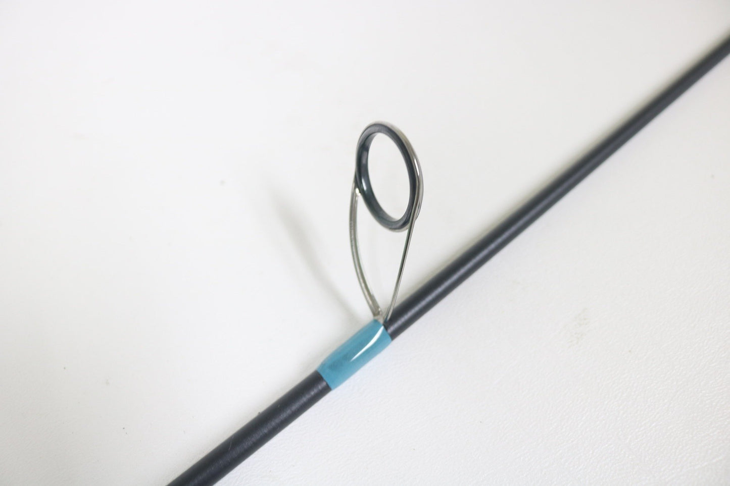 Close-up of a G. Loomis NRX+ 782s SJR 6'6" Medium Used Spinning Rod in excellent condition, featuring a metal line guide and blue tape wrap—eligible for our Rod and Reel Trade-In for store credit—shown on a white background.