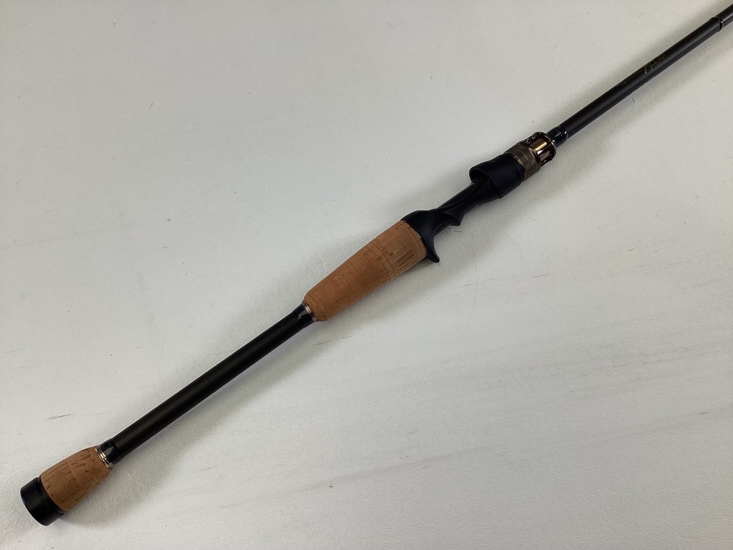 The Megabass Destroyer P5 F3.1/2-70X Used Casting Rod by Megabass, featuring cork handles and a black reel seat, is shown lying diagonally on a white surface in excellent condition.