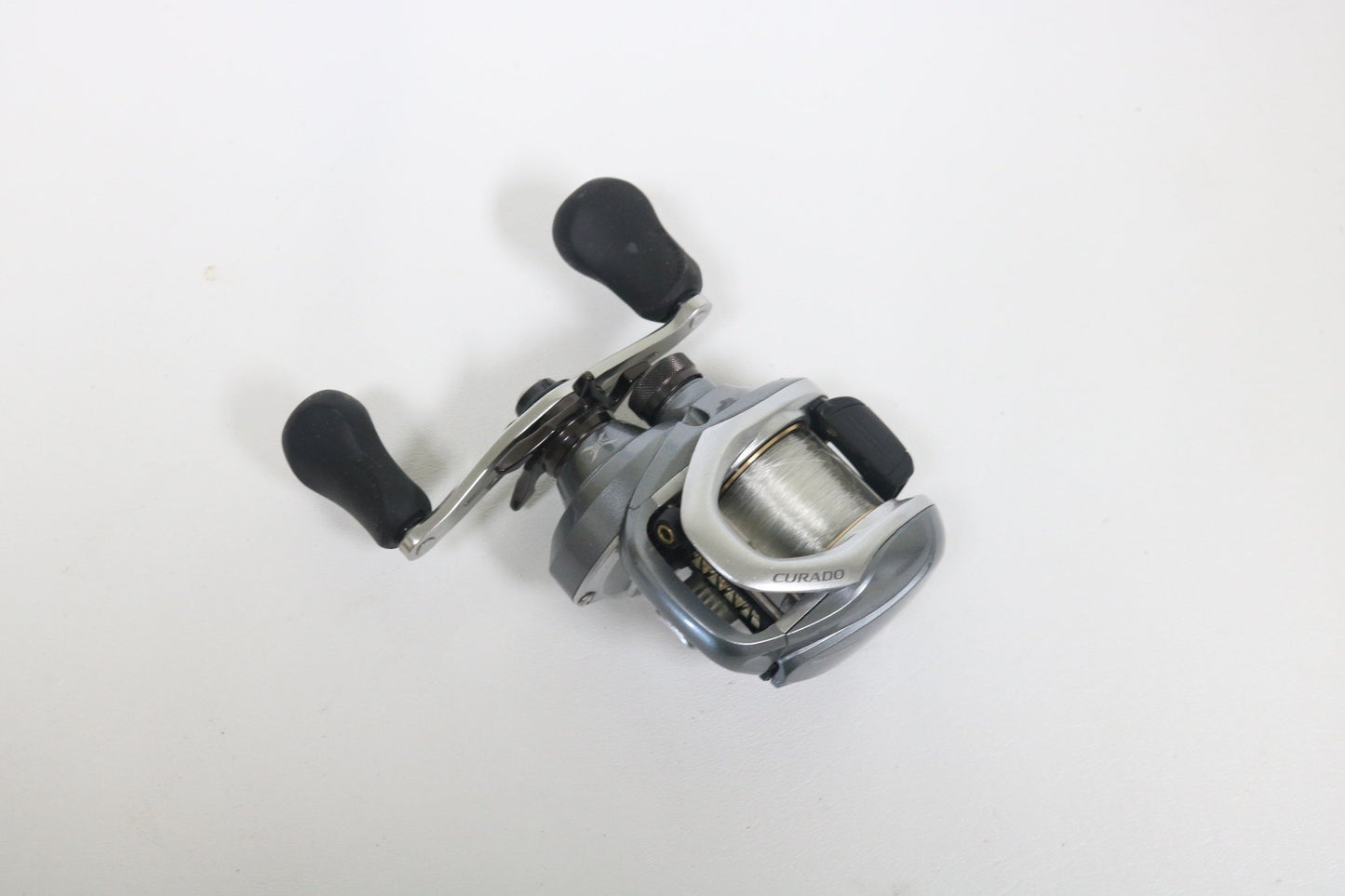 A Shimano Curado I 200PG 5.5:1 Used Casting Reel in excellent condition, featuring a silver and black design with two black handles, is displayed on a plain white surface—ideal for anglers exploring Used Gear or our Rod and Reel Trade-In.