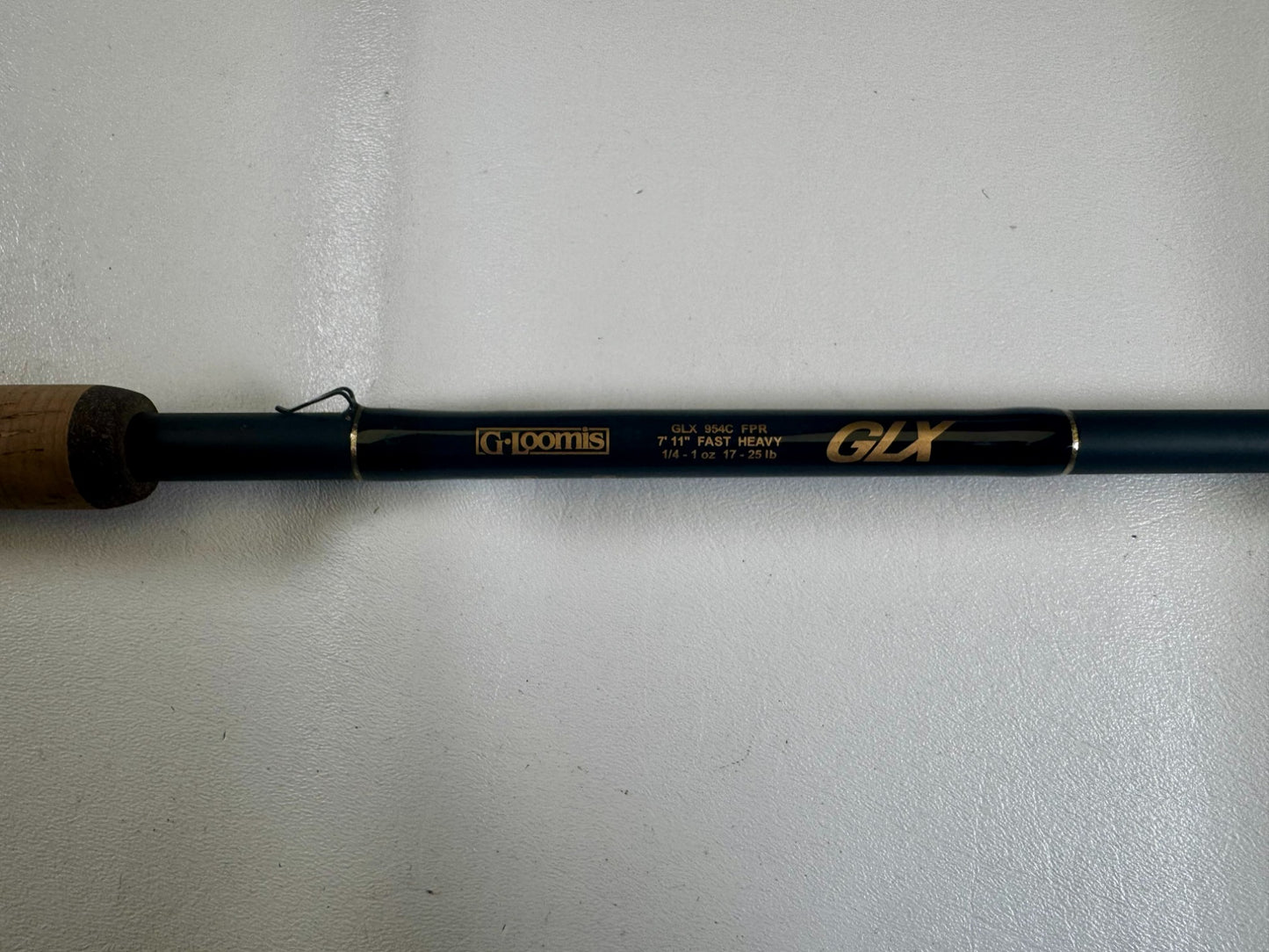 A close-up of the G. Loomis 24 GLX 954c FPR 7'11" Heavy Used Casting Rod in excellent condition, showing gold model details on a dark rod with a cork handle—ideal for those interested in used gear or our Trade-In Program.