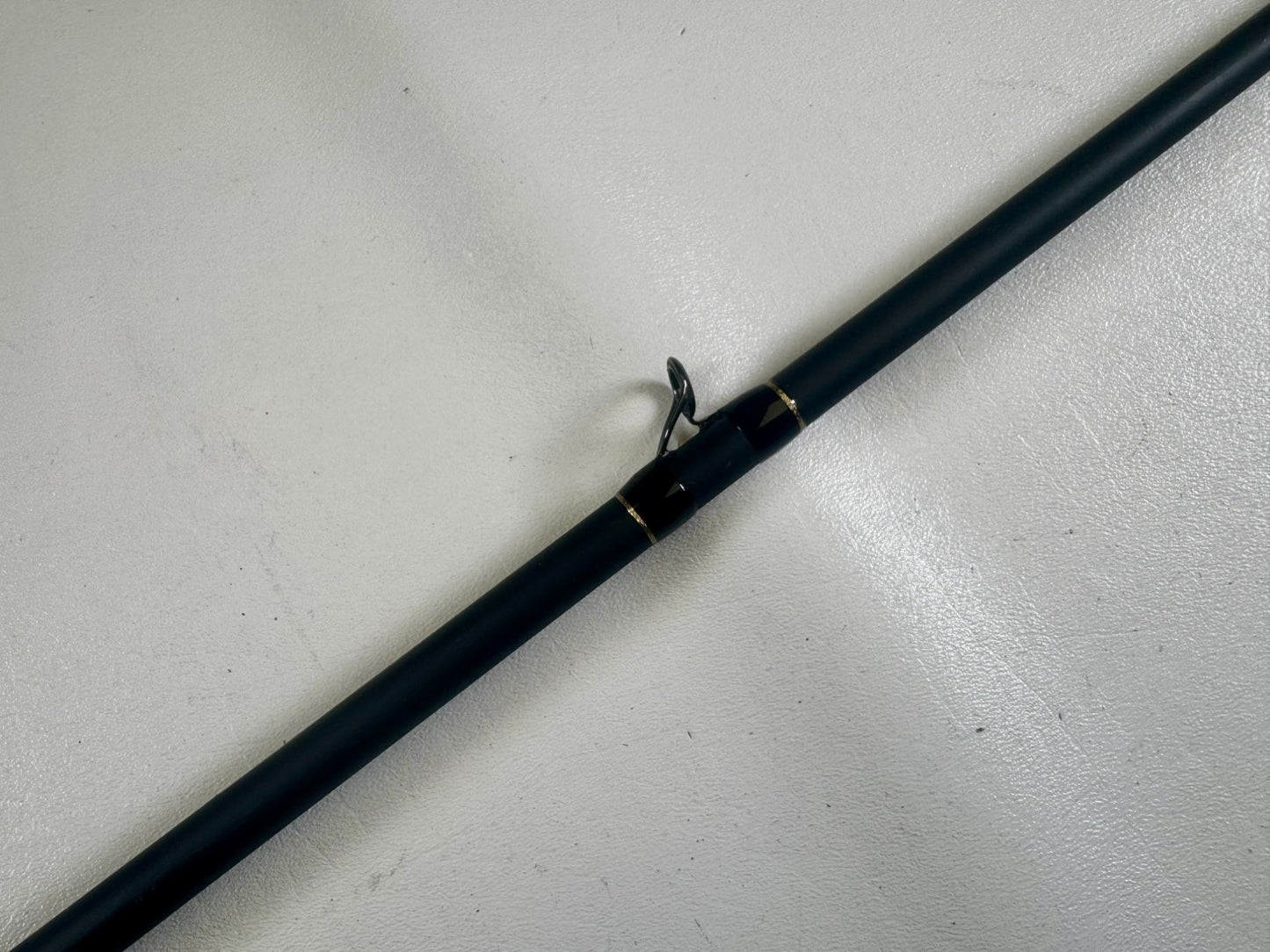 A close-up of a G. Loomis 24 GLX 954c FPR 7'11" Heavy used casting rod in excellent condition, showing a single guide ring, resting on a light-colored textured surface.