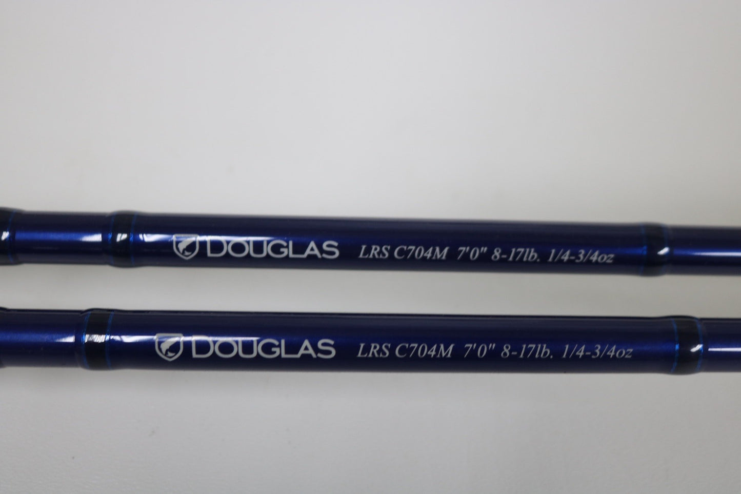 Two blue Douglas LRS C704M Casting Rods in very good used condition, each with white "DOUGLAS LRS C704M 7'0" 8-17lb. 1/4-3/4oz" text, ideal for anglers upgrading through our Trade-In or looking for quality pre-owned gear. Shown on a white background.
