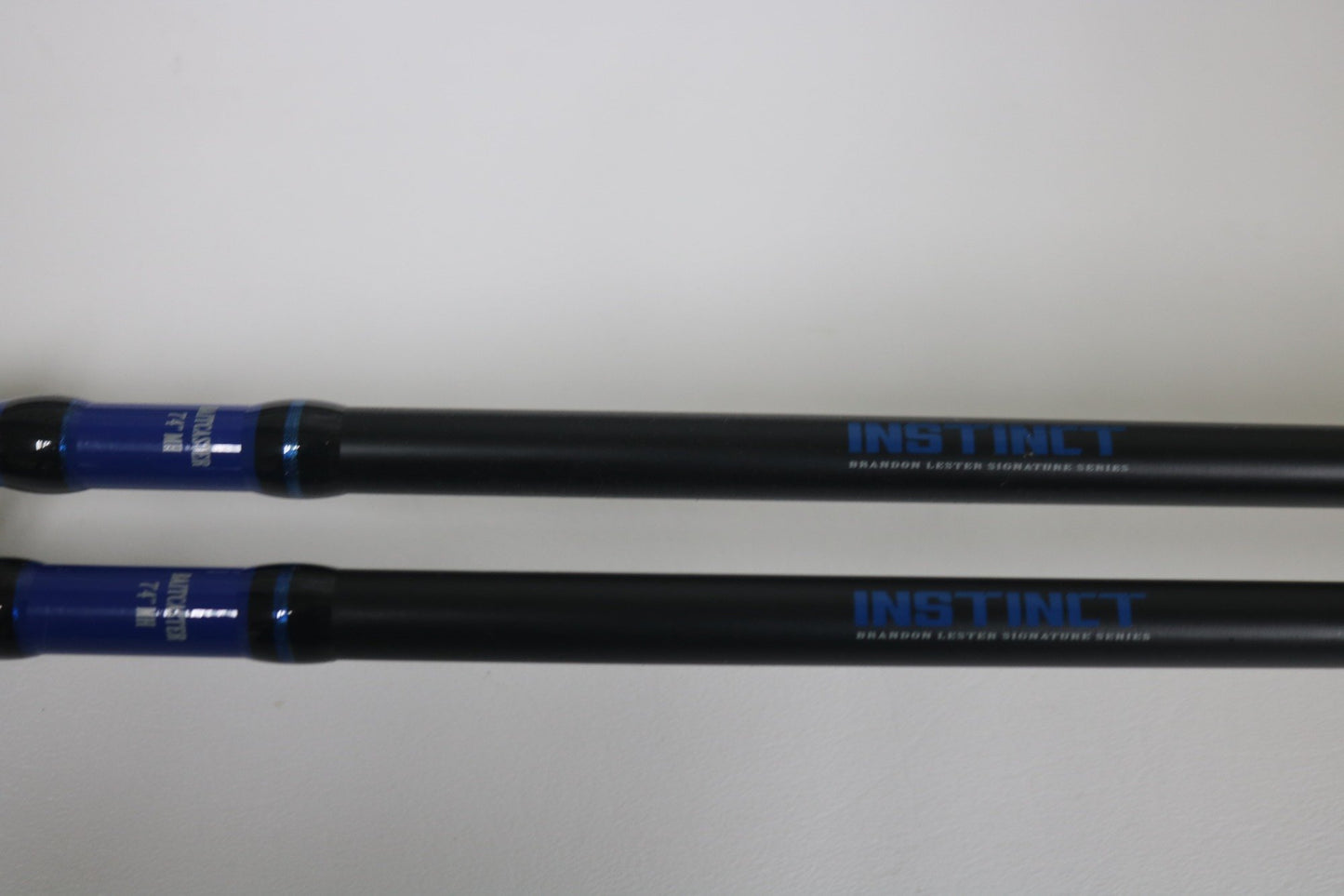 Two Mustad BLF Instinct 7'4" Medium Heavy Casting Rods in very good used condition lie parallel on a white surface. Trade in your used gear through our Nation's Best Rod and Reel Trade-In Program for store credit.