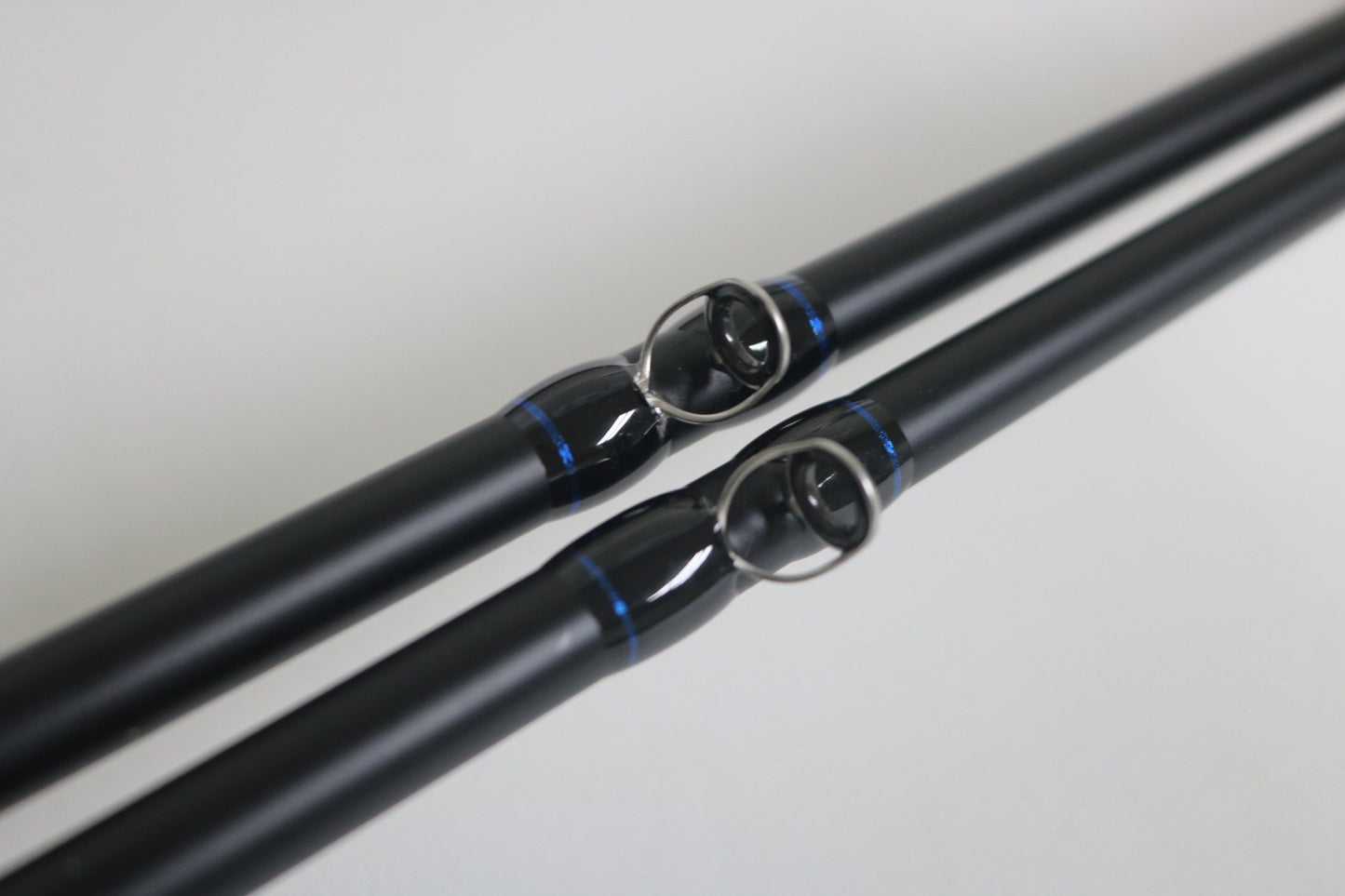 Two Mustad BLF Instinct 7'4" Medium Heavy Casting Rods in black with blue accents are shown parallel, highlighting their line guides—ideal for those seeking quality gear through the Nation’s Best Rod and Reel Trade-In Program.