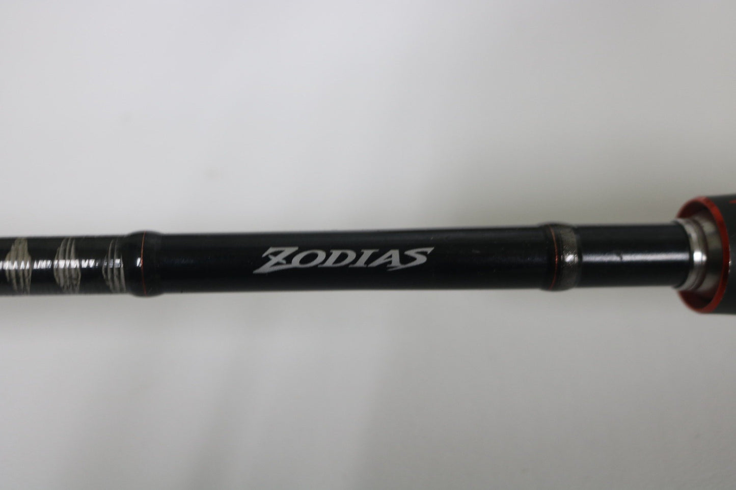 A close-up of a Shimano Zodias ZDC610MA 6'10" Medium used casting rod in very good condition, with "ZODIAS" in white on its black side. Ideal for Rod and Reel Trade-In Program or those shopping used Shimano gear. Light, plain background.