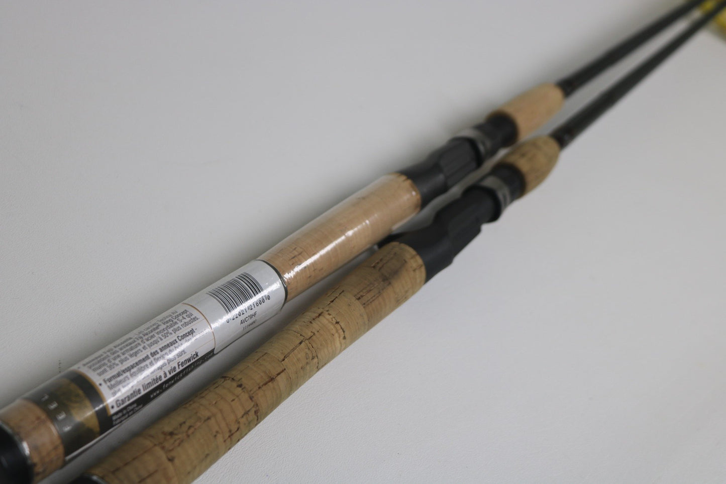 Two Fenwick Techna Av AVC79HF and AVC71HF Casting Rods in very good used condition are shown side by side on a white surface, one with a barcode label for the Rod and Reel Trade-In Program; both display authentic worn cork handles.