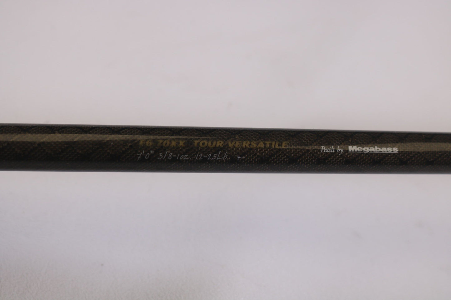 A close-up of the Megabass Orochi XX F6-70XX Tour Versatile 7'0" Heavy rod with "Built by Megabass" etched on its textured dark surface. Ideal for our Rod and Reel Trade-In Program, offering store credit for well-maintained used gear.