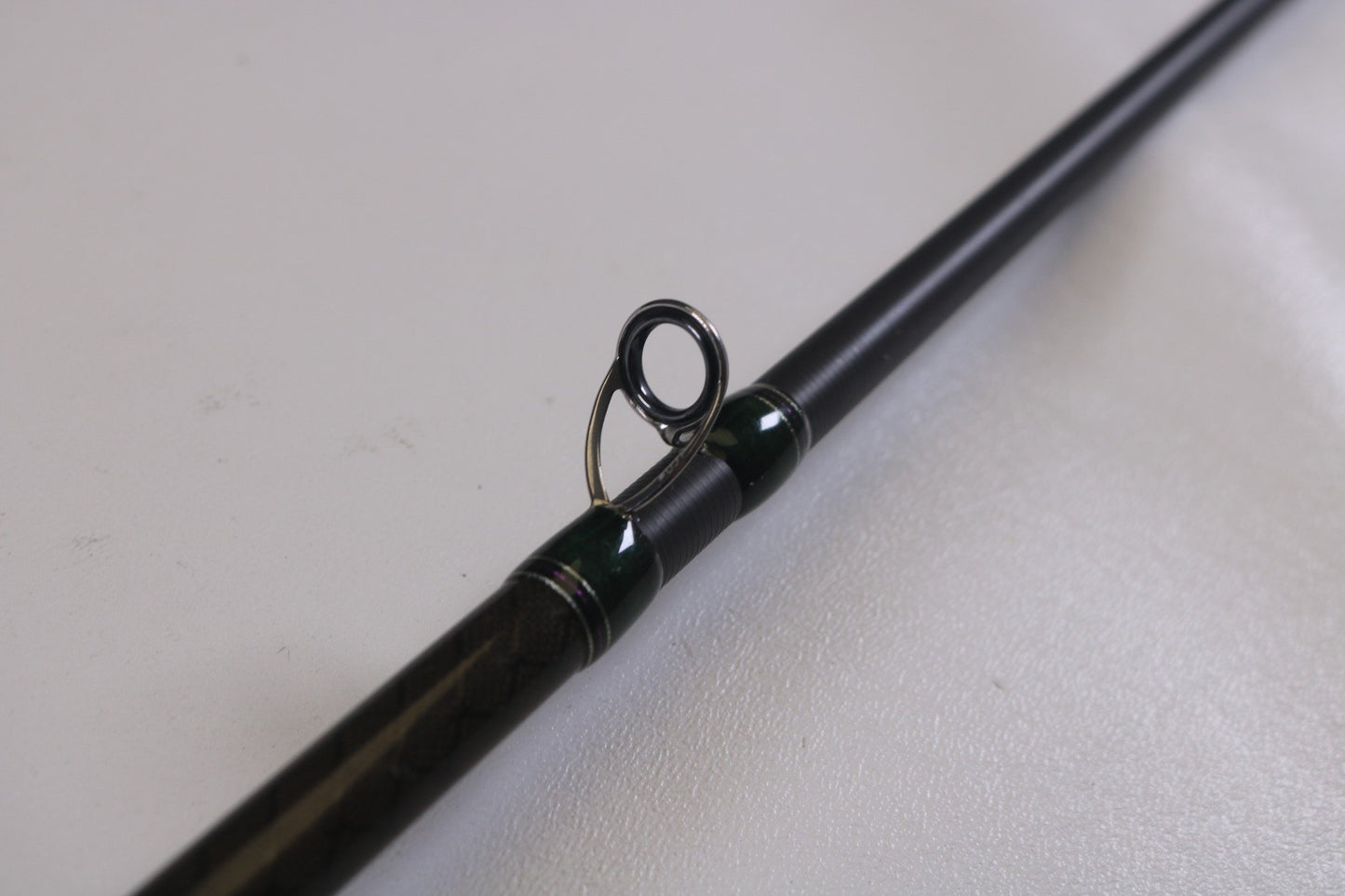 A close-up of the line guide on a Megabass Orochi XX F6-70XX 7'0" Heavy casting rod, part of our Rod and Reel Trade-In Program. The circular guide has a shiny metal finish, and the sleek dark rod rests on a light surface—perfect for assessing used gear conditions.