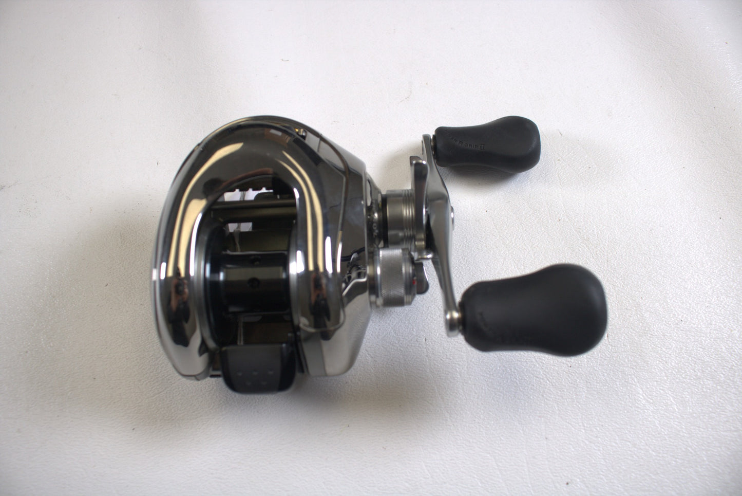 A Shimano Calais 200DC 7.0:1 baitcasting reel in excellent used condition, featuring two black ergonomic handles, is displayed on a white surface.