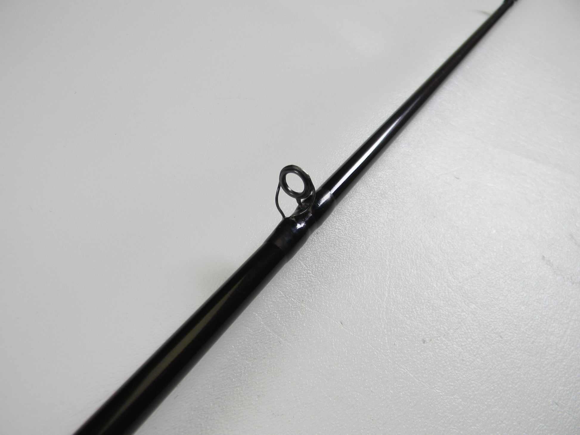 Close-up of a St. Croix Mojo Bass MJC68MF Jerkbait 6'8" Medium casting rod tip in black, featuring a single guide ring on a light surface, ideal for those seeking an upgrade through our trade-in program to earn store credit.
