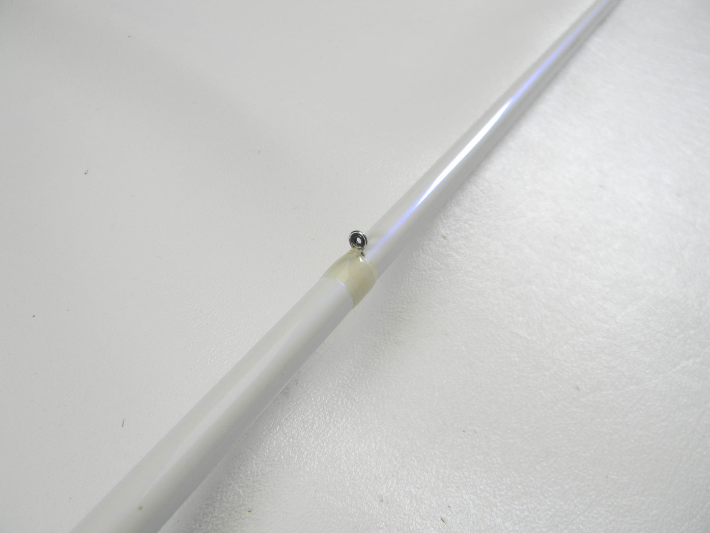 Close-up of a Duckett White Ice DFWI711MHCC Byron Velvick 7'11" Medium Heavy Lure Launcher casting rod against a white background, perfect for a Rod and Reel Trade-In. The slender white rod, in very good used condition, features a small black hinge wrapped in yellowish tape.