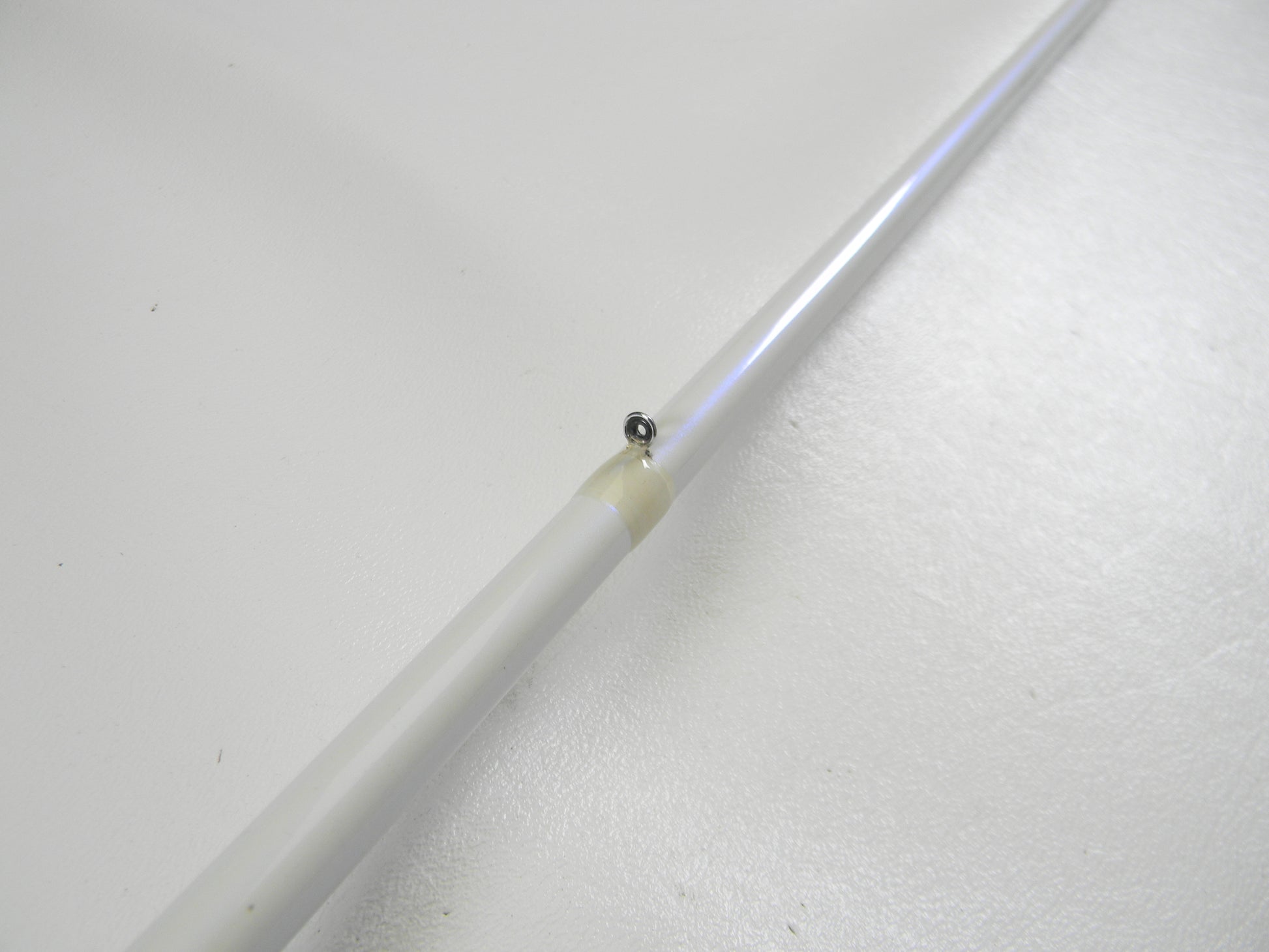 Close-up of a Duckett White Ice DFWI711MHCC Byron Velvick 7'11" Medium Heavy Lure Launcher casting rod against a white background, perfect for a Rod and Reel Trade-In. The slender white rod, in very good used condition, features a small black hinge wrapped in yellowish tape.