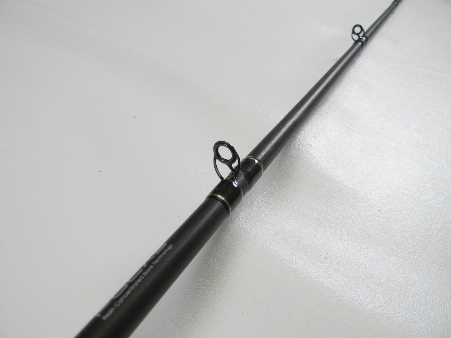 The Lew's Signature Series TLS76H Pitching 7'6" Heavy Used Casting Rod, eligible for our Rod and Reel Trade-In Program, is showcased lying on a white surface. The image focuses on its evenly spaced multiple line guides with a sleek black finish, highlighting this quality gear in excellent condition.