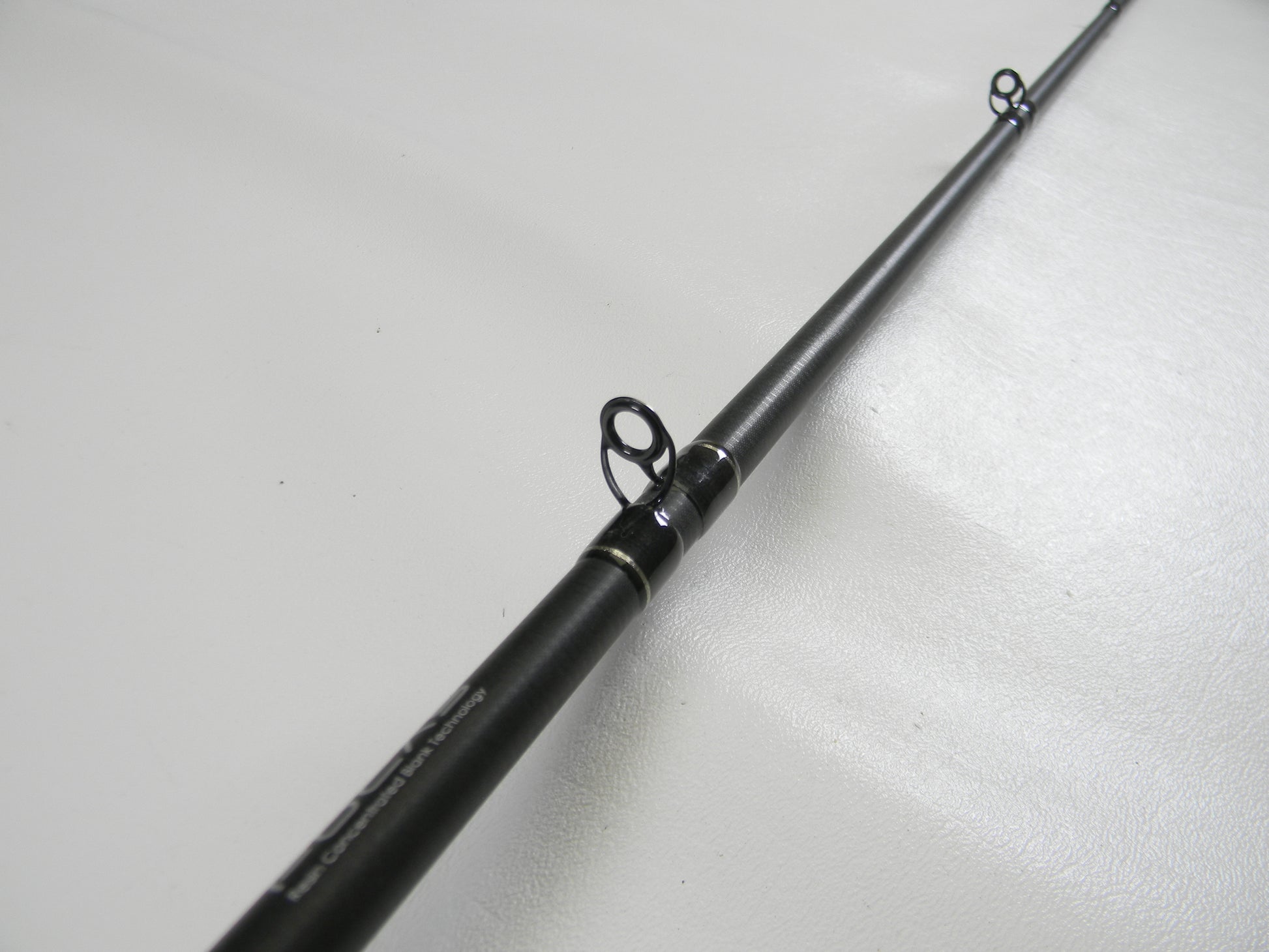 The Lew's Signature Series TLS76H Pitching 7'6" Heavy Used Casting Rod, eligible for our Rod and Reel Trade-In Program, is showcased lying on a white surface. The image focuses on its evenly spaced multiple line guides with a sleek black finish, highlighting this quality gear in excellent condition.
