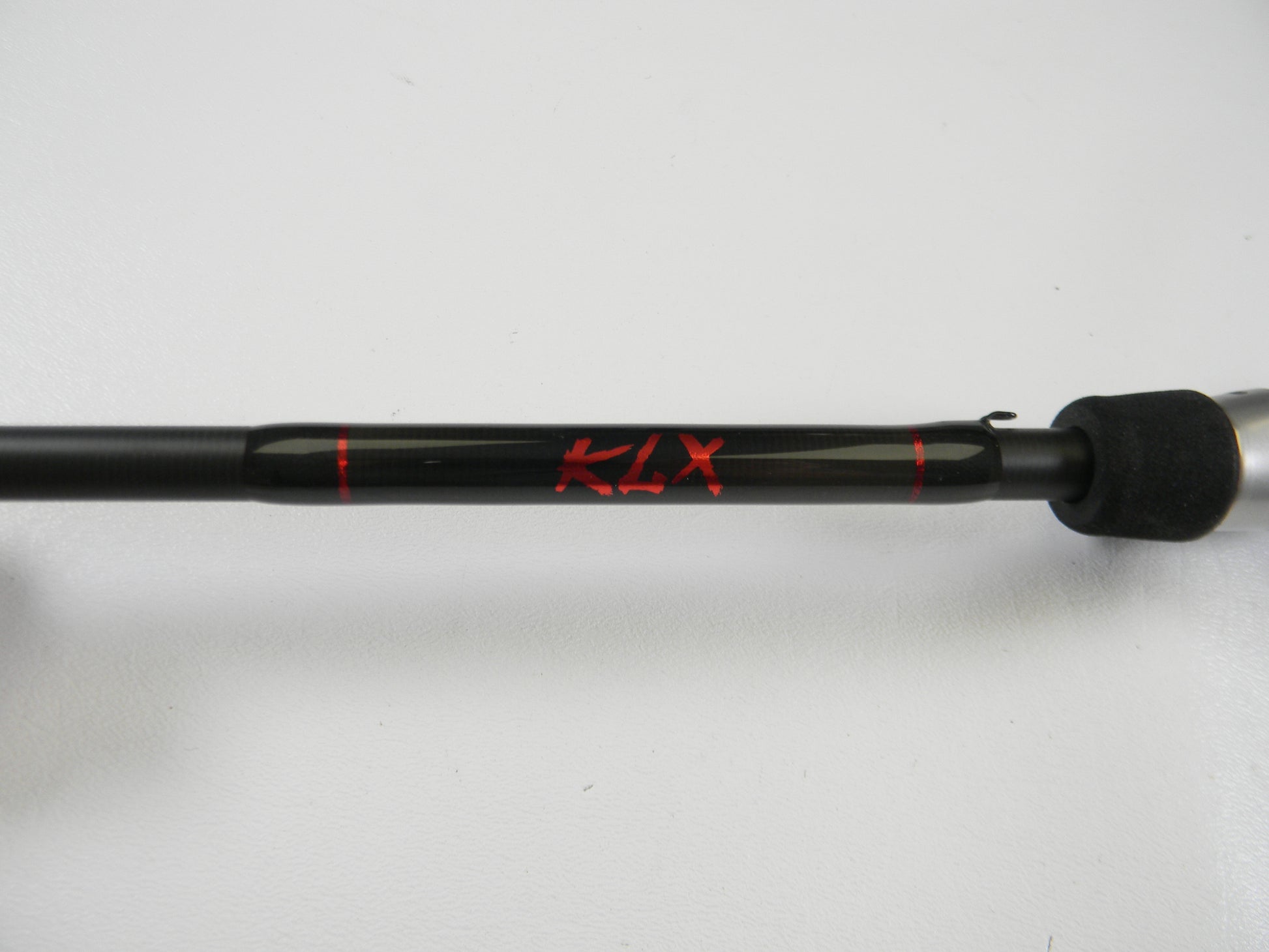 A black Kislter KLX 7'0" Medium Heavy casting rod with "KLX" in red and a textured grip is set against a white backdrop. Ideal for our Rod and Reel Trade-In Program—trade your used gear for store credit.