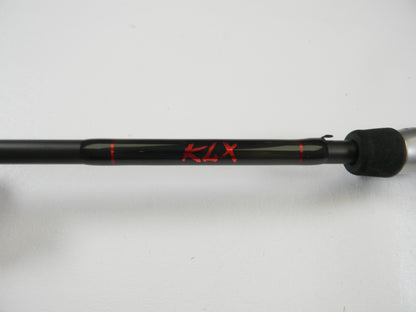 A black Kislter KLX 7'0" Medium Heavy casting rod with "KLX" in red and a textured grip is set against a white backdrop. Ideal for our Rod and Reel Trade-In Program—trade your used gear for store credit.