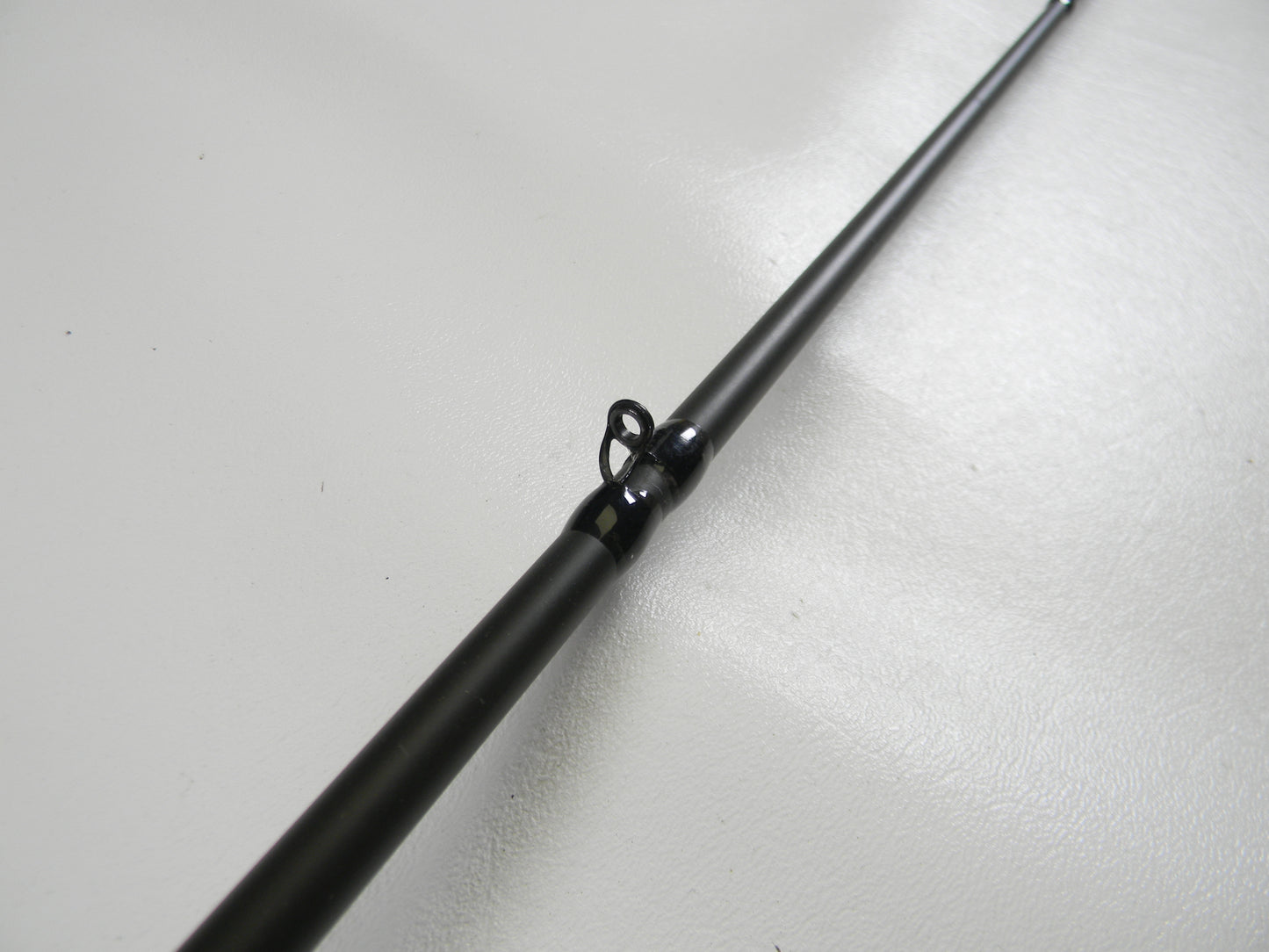 Close-up of a Cashion P84469b 6'9" medium heavy used casting rod in good condition with a shiny metallic eyelet, resting on a smooth white surface. This product may qualify for our rod and reel trade-in program, offering potential store credit.