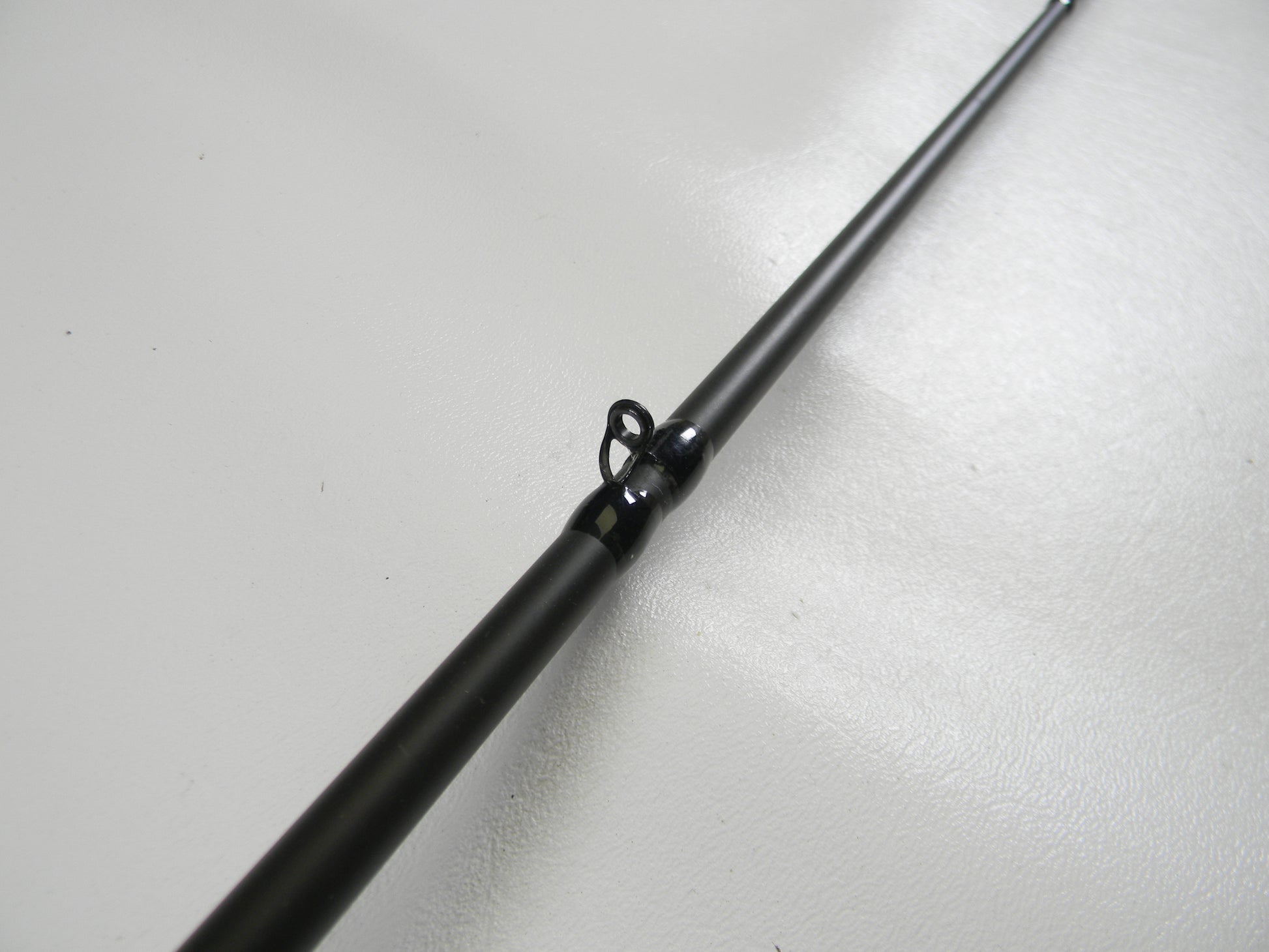 Close-up of a Cashion P84469b 6'9" medium heavy used casting rod in good condition with a shiny metallic eyelet, resting on a smooth white surface. This product may qualify for our rod and reel trade-in program, offering potential store credit.