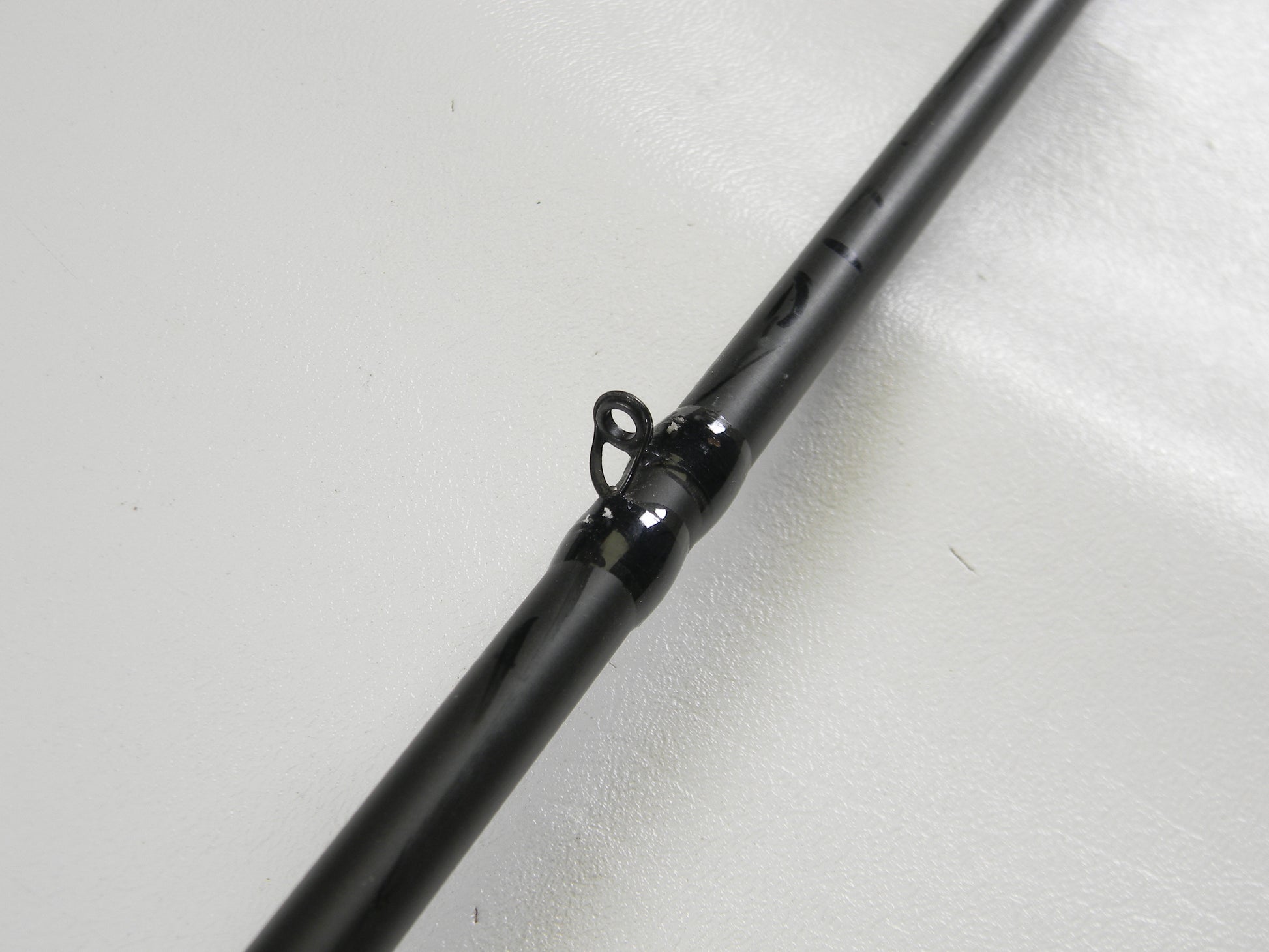 A close-up of a Cashion F90474b 7'4" Medium Heavy used casting rod in very good condition, lying on a white surface, highlights a black line guide loop. This fishing rod may qualify for our Rod and Reel Trade-In Program.