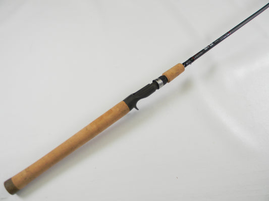 The Falcon EVO VFC-7-173 7'3" Heavy casting rod, in excellent used condition with a wooden handle and black reel seat, is laid diagonally on a white background. Available through our Rod and Reel Trade-In Program, it features metal guides along its length.