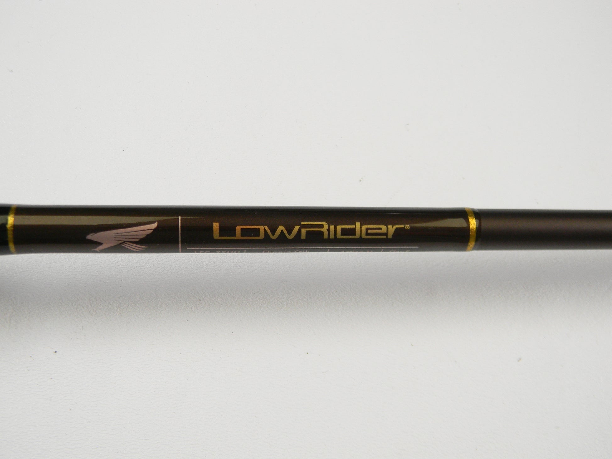 Close-up of the Falcon Lowrider LFC-72HH Flippin Stik 7'2" Heavy in black with gold accents, featuring "LowRider" and an eagle logo. Perfect for trade-in programs, this rod offers anglers store credit on used gear. Set against a plain white surface, it highlights its sleek design.