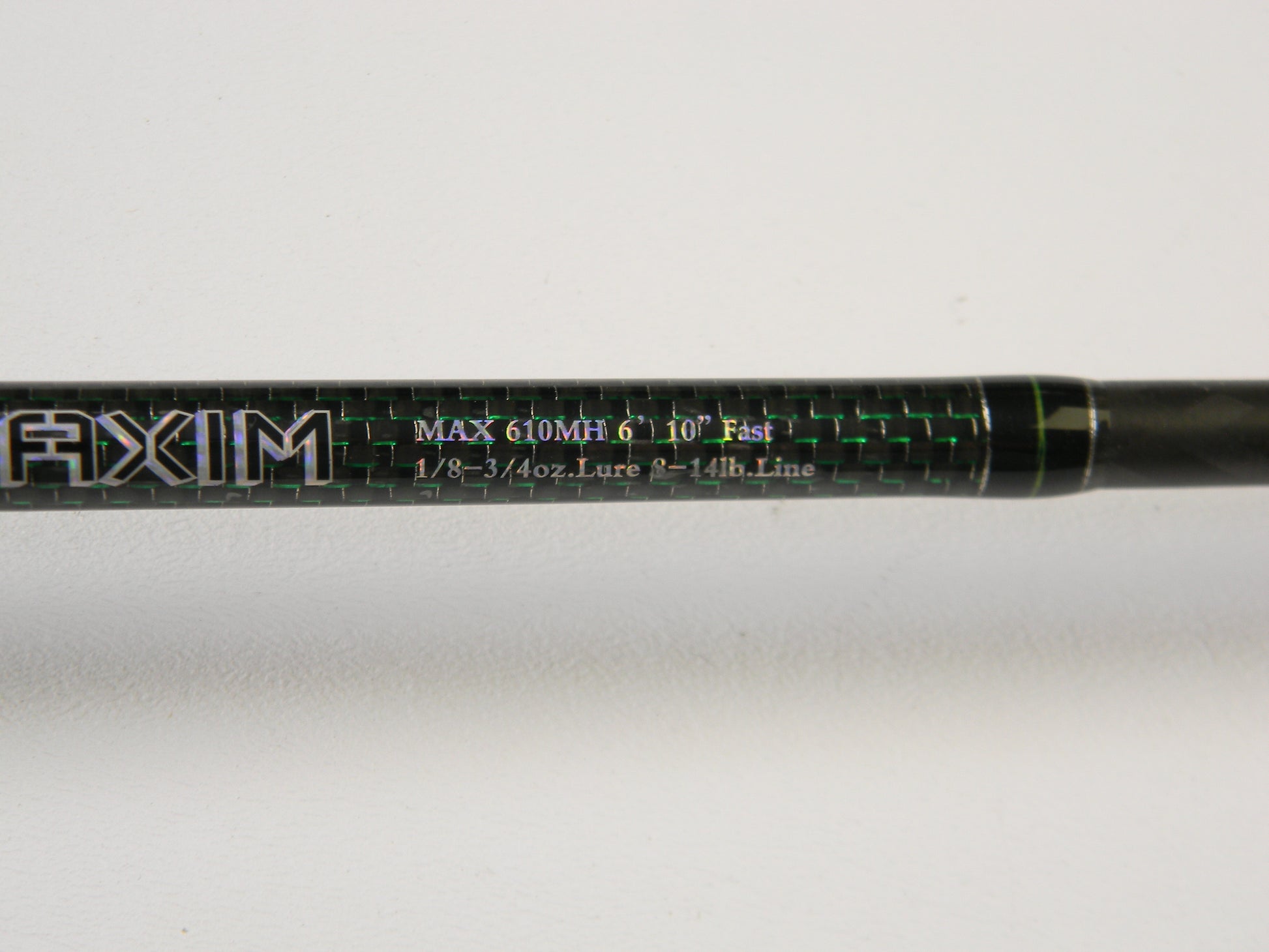 Close-up of a Phenix Maxim PHX-MAX-C610MH 6'10" Medium Heavy casting rod with "MAX 610MH 6'10" Fast 1/8 - 3/4oz. Lure 6 - 14lb. Line" in green and white, featuring "AXIM" prominently. Ideal for our Rod and Reel Trade-In Program—upgrade your used gear for store credit today!.