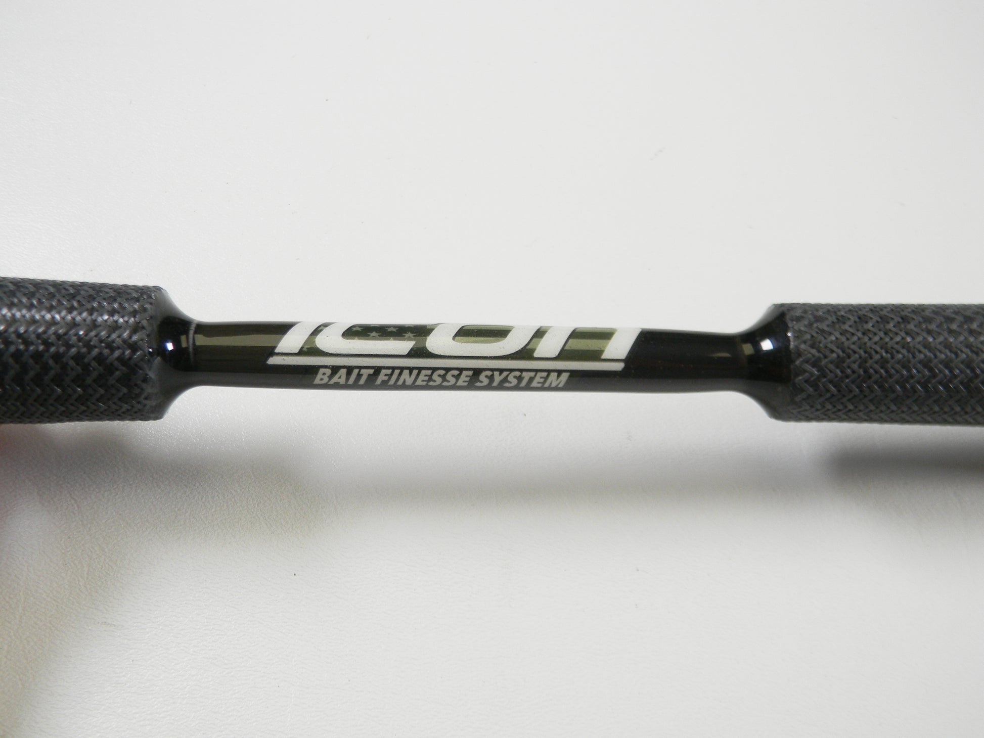 Close-up of Cashion Icon Series iBFS610MLF 6'10" Medium Light casting rod's handle with "ICON BAIT FINESSE SYSTEM" written in white. The textured dark grips are perfect for any angler considering a Rod and Reel Trade-In for store credit.