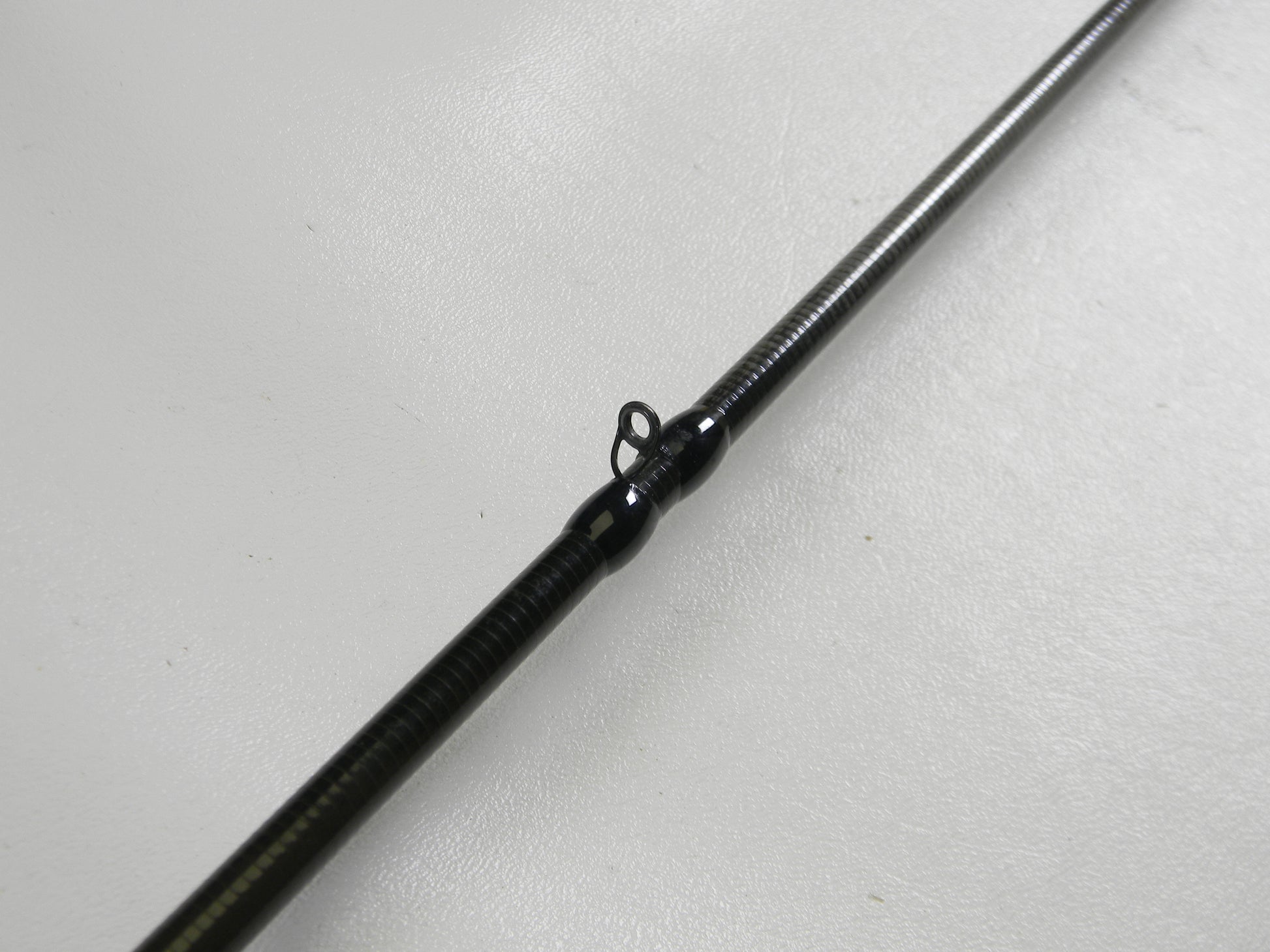 Check out the close-up of the Cashion Icon Series iBFS610MLF 6'10" Medium Light - Used Casting Rod, featuring a metal guide loop, part of our used gear selection. This dark-colored rod rests on a light surface and is perfect for those utilizing our Rod and Reel Trade-In program for store credit.