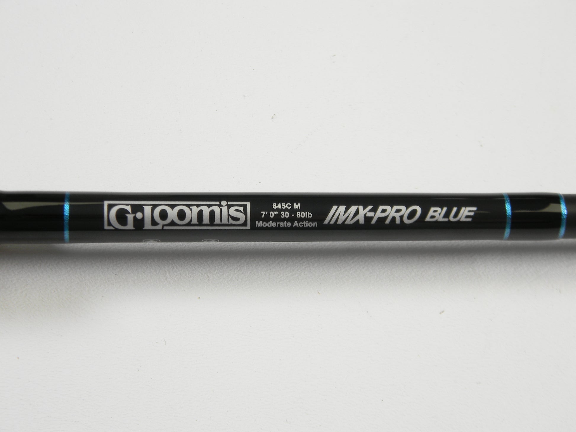 A close-up of a used G. Loomis IMX-PRO Blue 845C M 7'0" Heavy Casting Rod in excellent condition, shown on a white background with blue accents. Ideal for those interested in used gear or our Rod and Reel Trade-In Program.