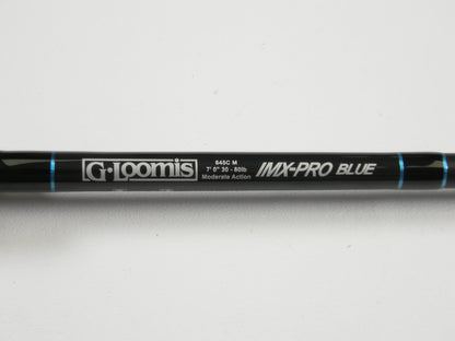 A close-up of a used G. Loomis IMX-PRO Blue 845C M 7'0" Heavy Casting Rod in excellent condition, shown on a white background with blue accents. Ideal for those interested in used gear or our Rod and Reel Trade-In Program.