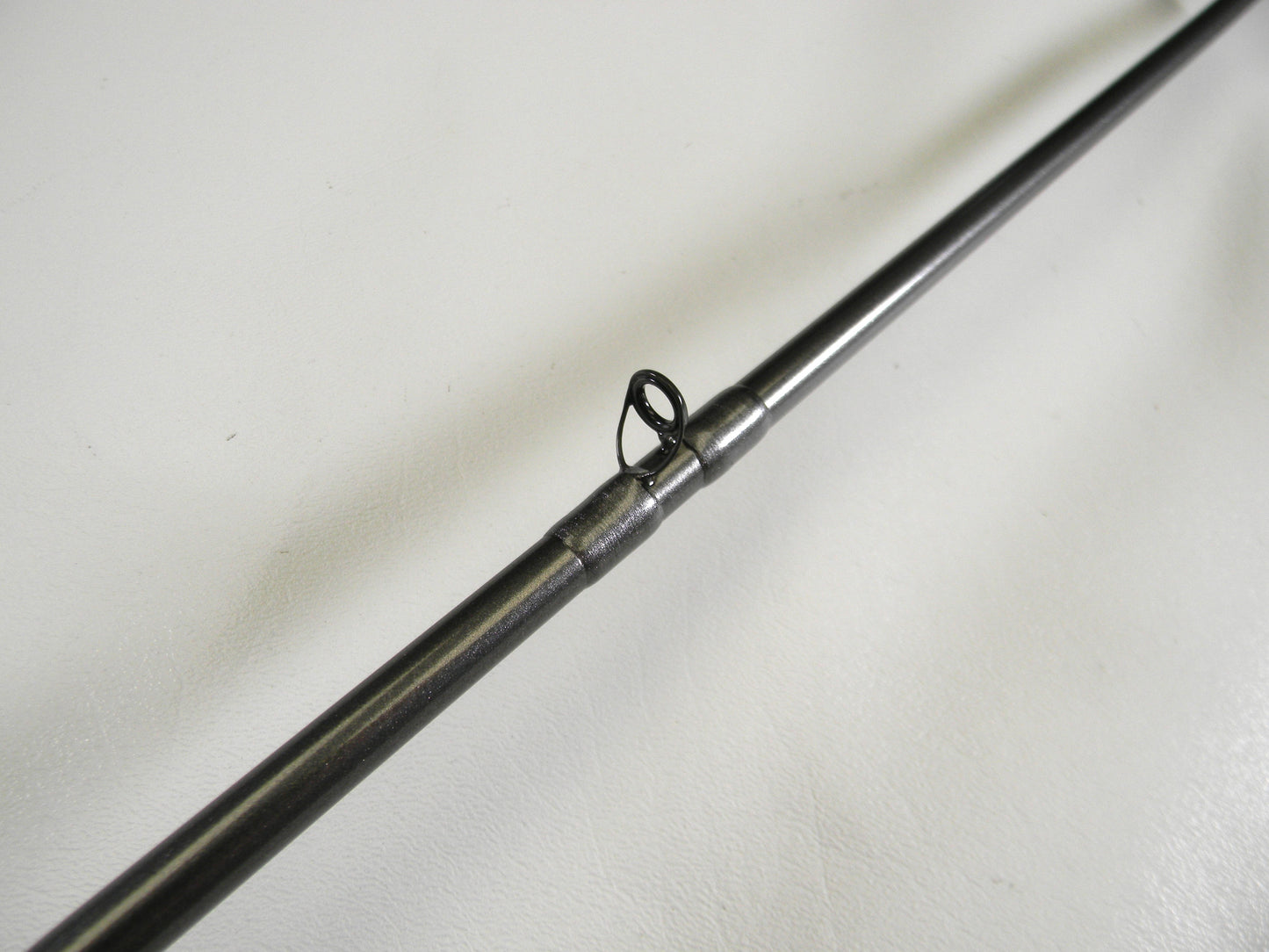 Close-up of a Daiwa Tatula Elite TTEL731HFB used casting rod's metal guide from our Trade-In Program. This circular loop directs the line along the rod's smooth metallic surface, set against a white background.