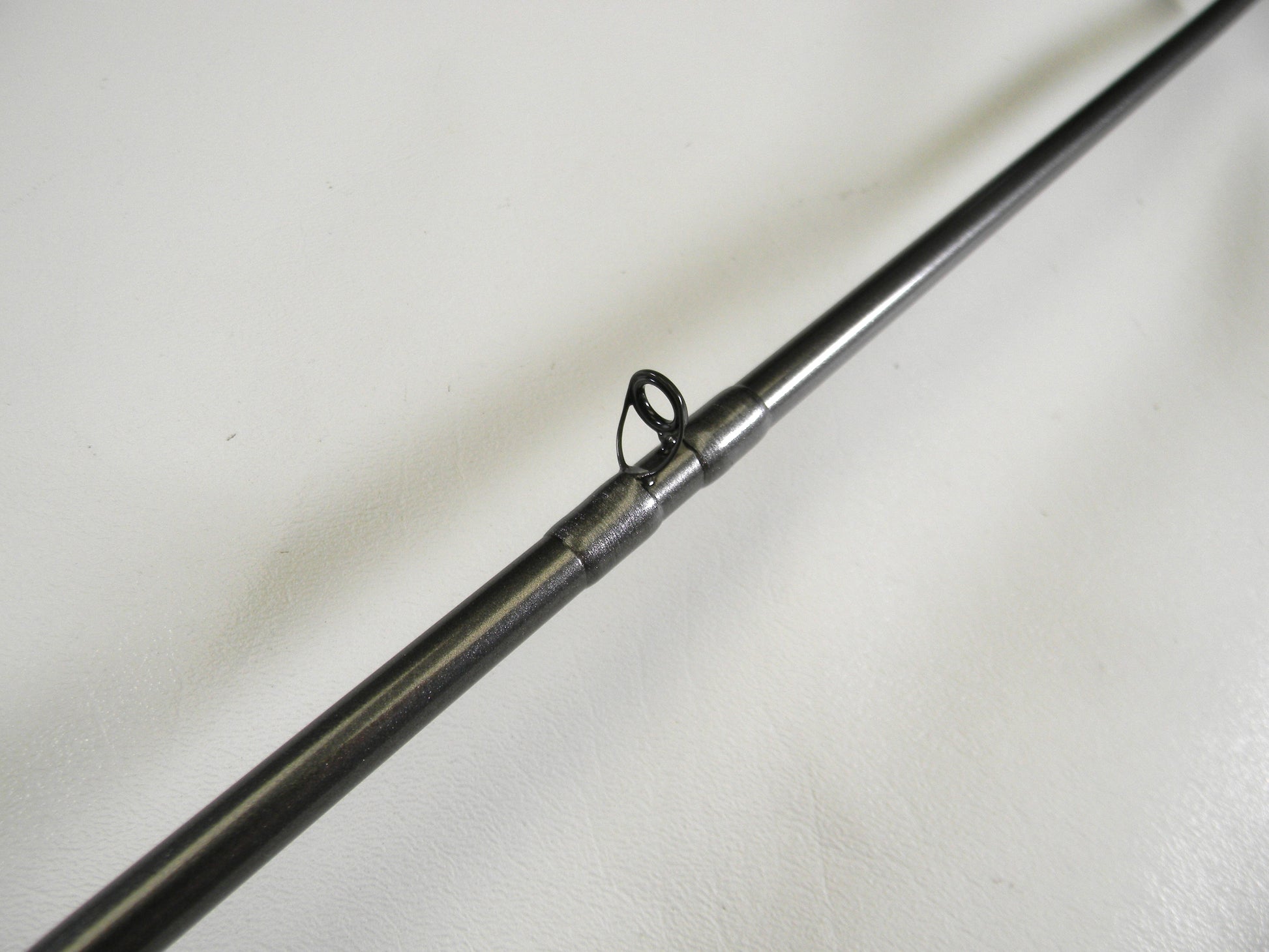 Close-up of a Daiwa Tatula Elite TTEL731HFB used casting rod's metal guide from our Trade-In Program. This circular loop directs the line along the rod's smooth metallic surface, set against a white background.