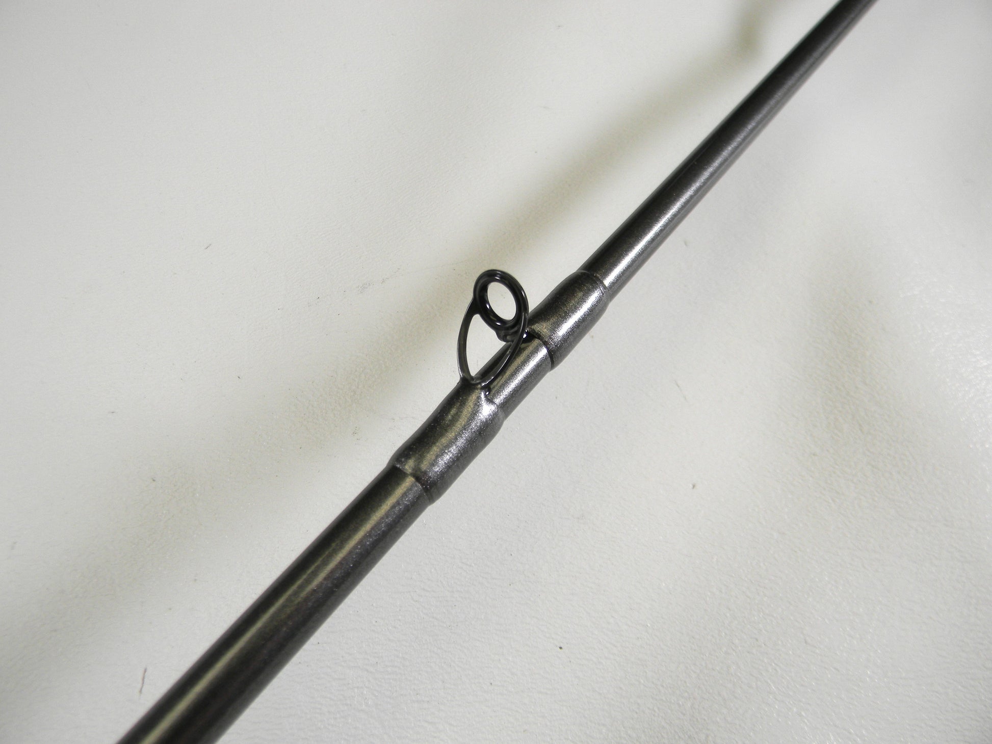 Close-up of a Daiwa Tatula Elite TTEL751MHFB, highlighting its metal guide ring on a dark pole against a light background. Perfect for our Rod and Reel Trade-In Program participants seeking quality gear, this 7'5" medium-heavy used rod is in mint condition.