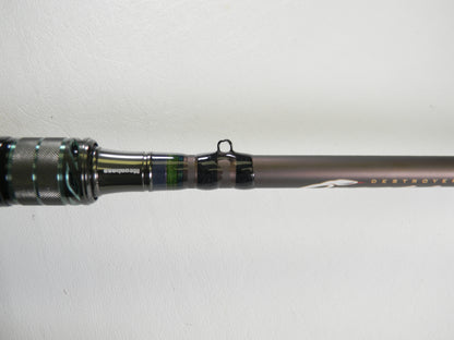 Close-up of a Megabass Orochi X10 F4-68XT Jabberwock 6'8" Medium Light casting rod handle and first line guide against white. The dark, metallic green-accented blank is ideal for our Rod and Reel Trade-In Program if upgrading used gear.