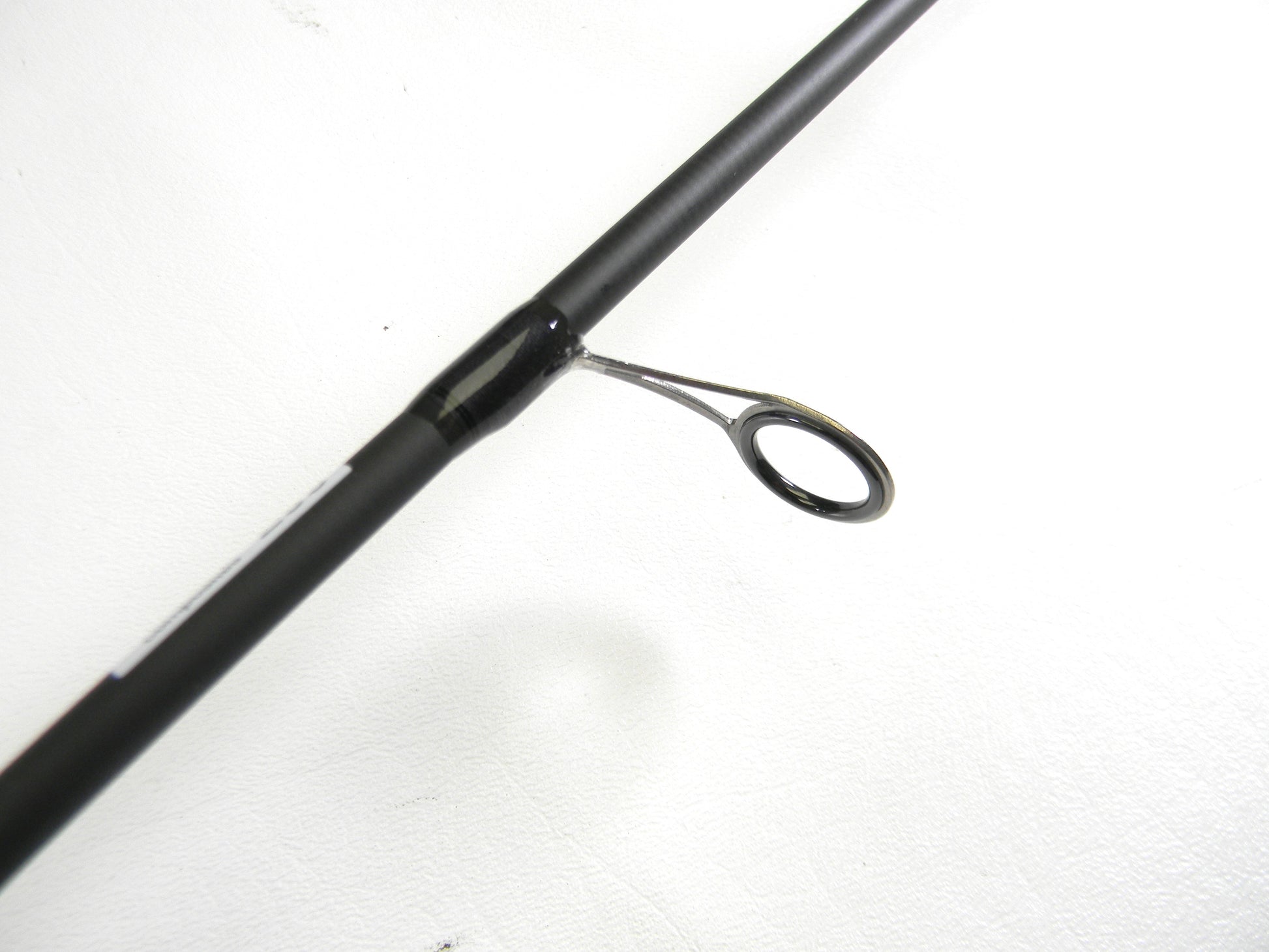 A close-up of an Abu Garcia Veritas Tournament VXTS610-4 6'10" Medium Light spinning rod guide against a white background is available through our Rod and Reel Trade-In program. The rod's black finish contrasts strikingly with the silver circular guide ring.
