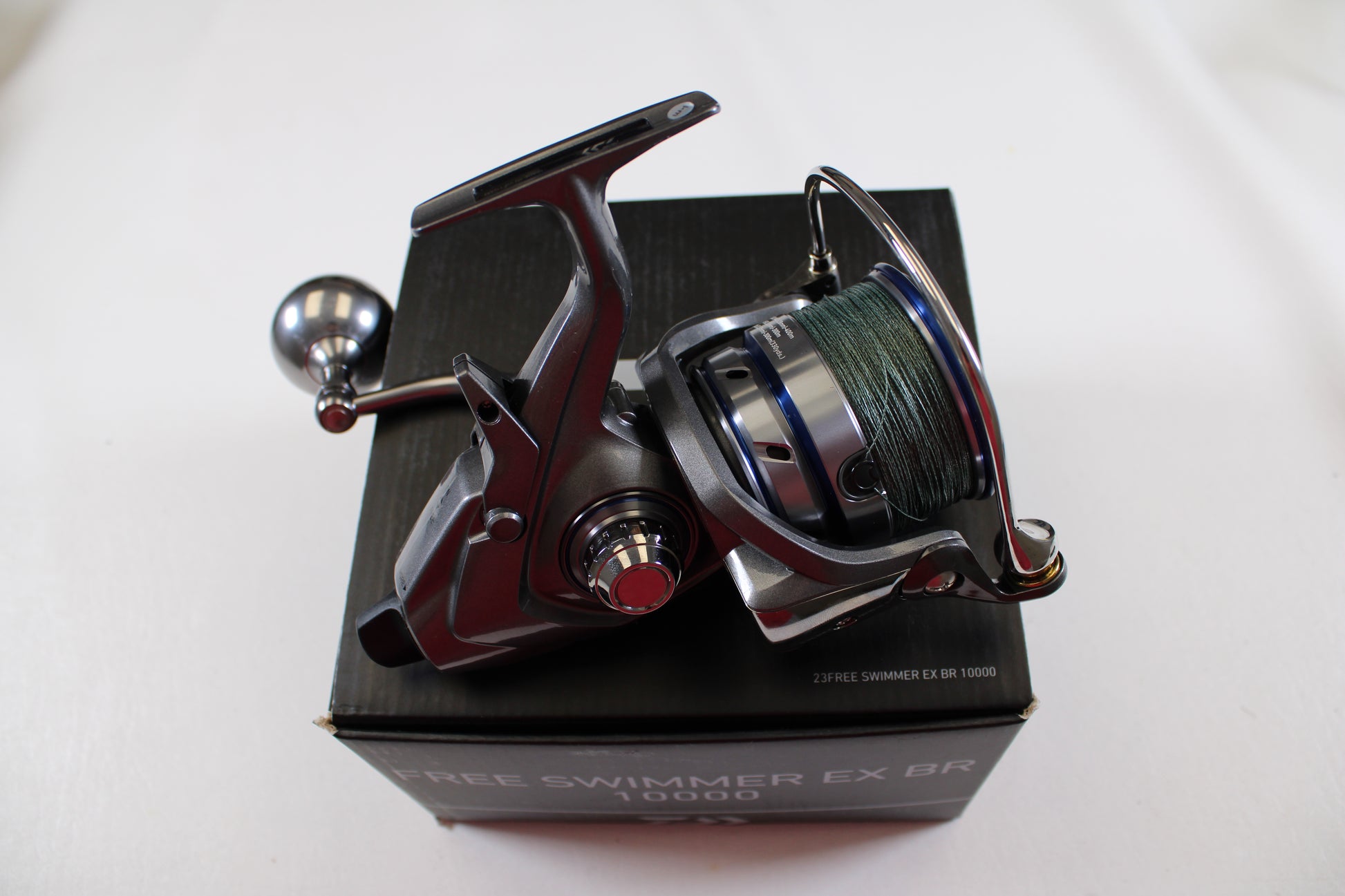 A Daiwa Free Swimmer EX BR 10000 used spinning reel in excellent condition, with a green fishing line spool, is mounted on a black box labeled "FREE SWIMMER EX BR 10000" against a plain white background—ideal for trade-in.
