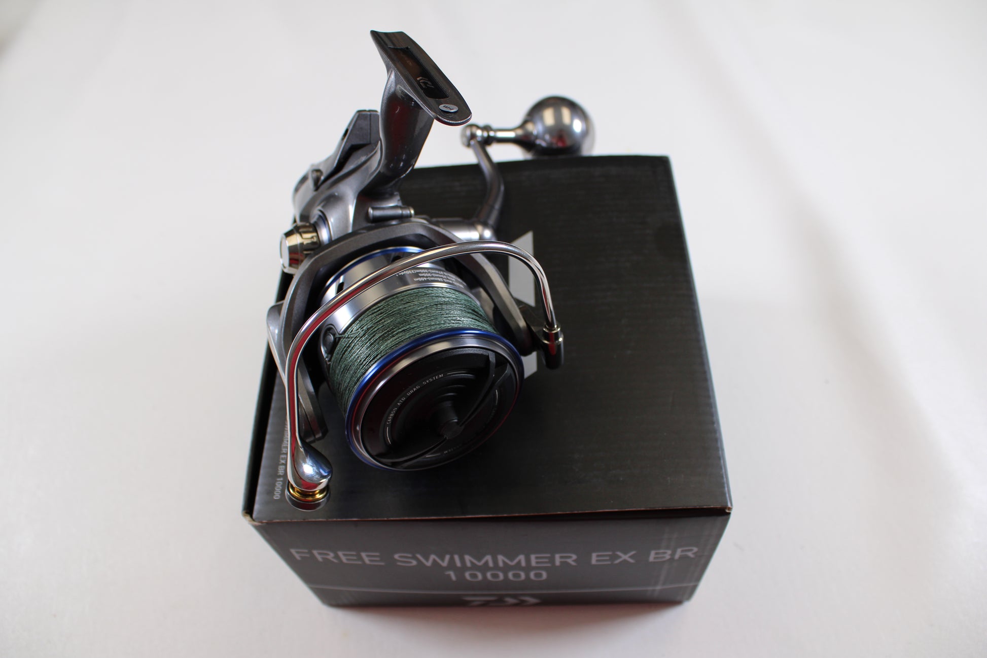 A used Daiwa Free Swimmer EX BR 10000 spinning reel with green line sits atop a black box, ideal for rod and reel trade-in programs; branded by Daiwa and set against a plain white background.